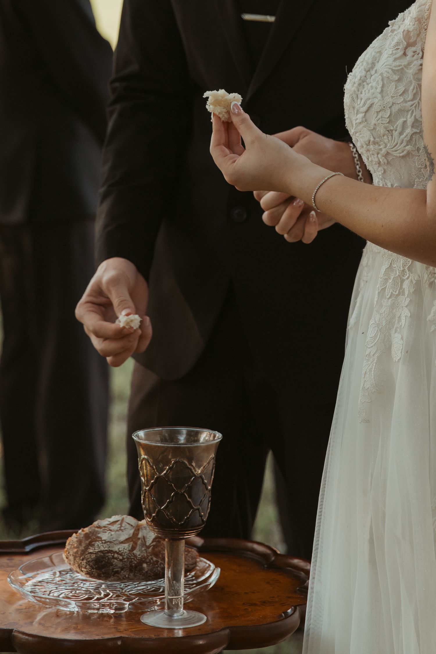 Bride and groom sharing communion bread and wine during outdoor wedding ceremony ritual.