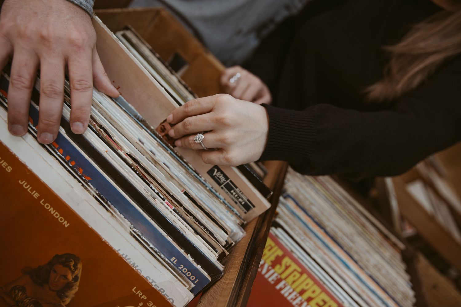 Hands browsing through a collection of vinyl records in warm lighting.