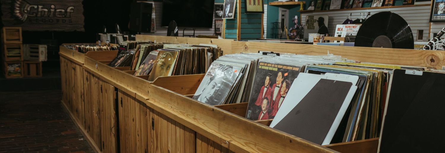 Vinyl records displayed in wooden bins at a vintage record store with worn wooden dividers.