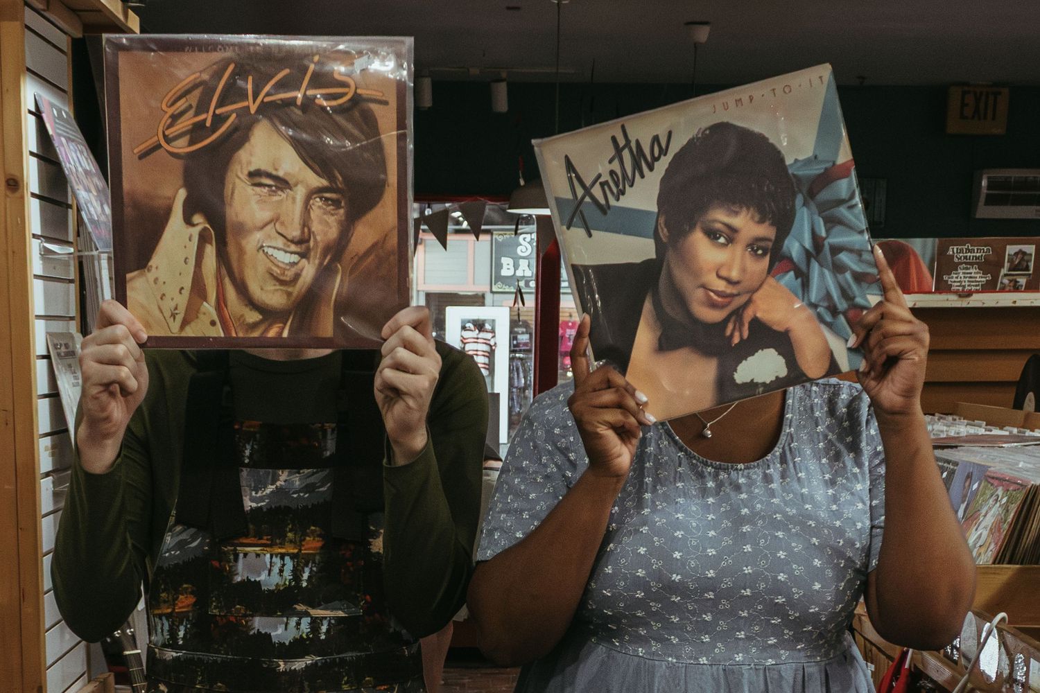 Two people hold up vintage vinyl record albums at a record store.
