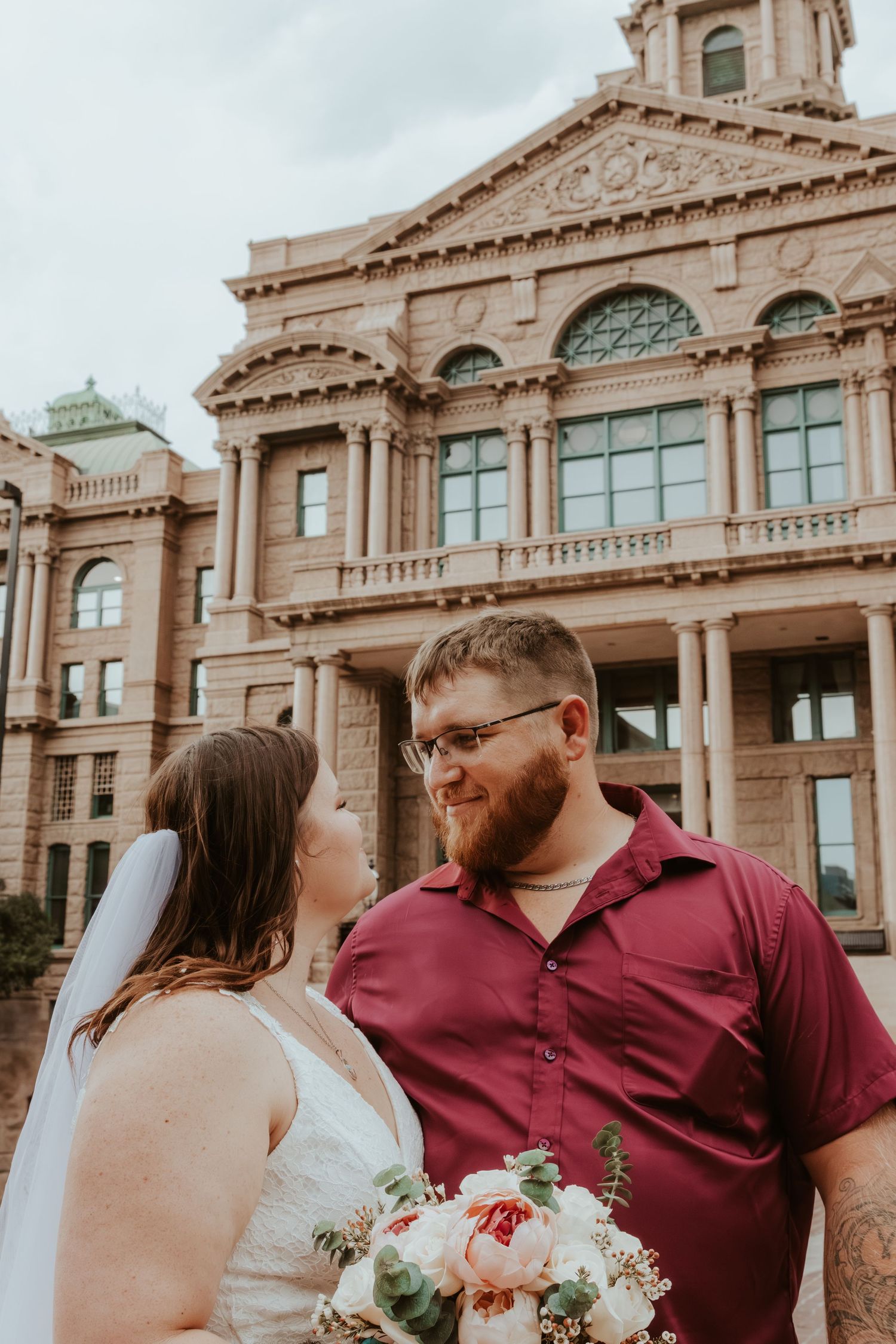 A couple poses for their wedding photos in front of a beautiful stone courthouse building.