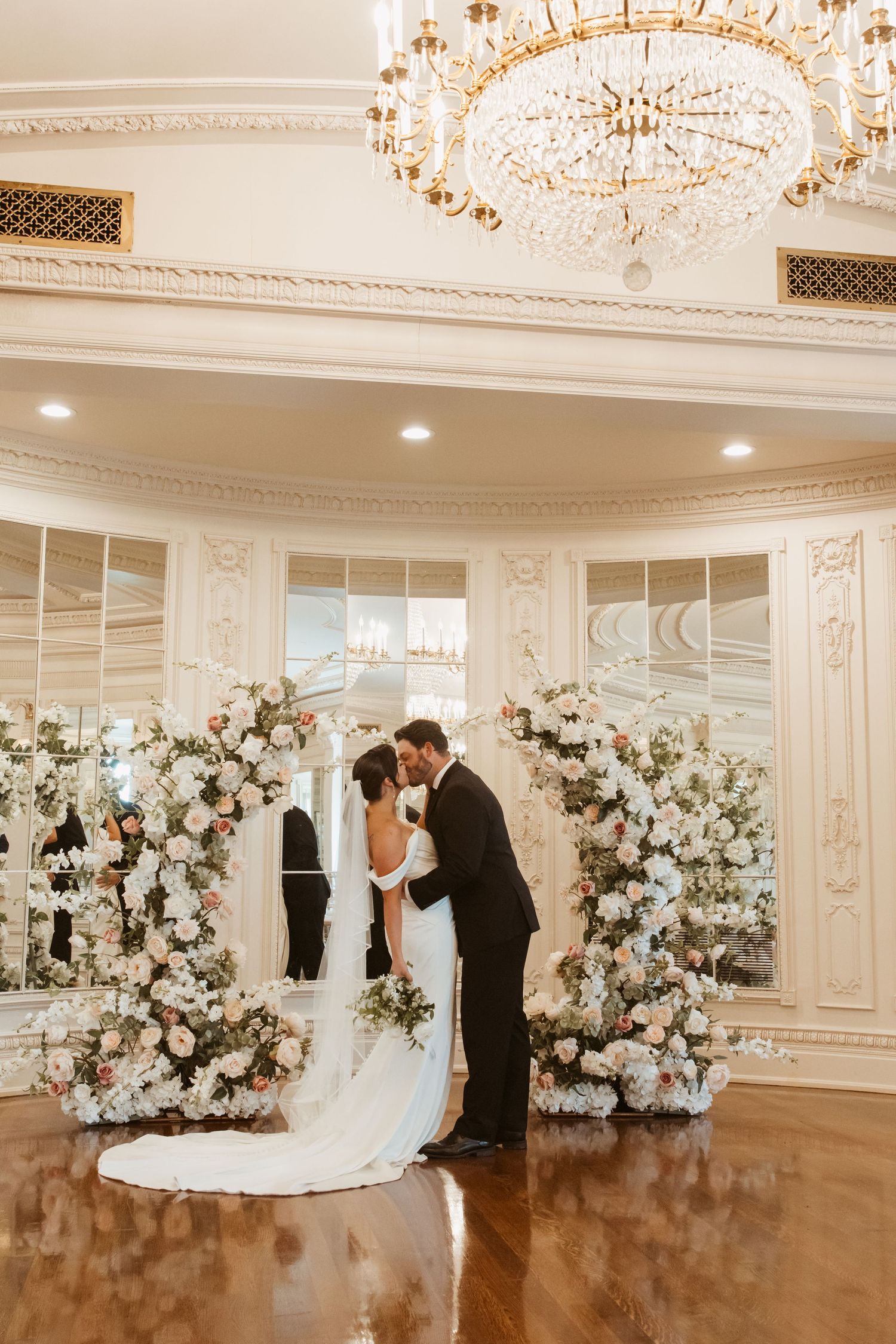 An elegant ballroom wedding scene with crystal chandeliers and white floral arrangements.