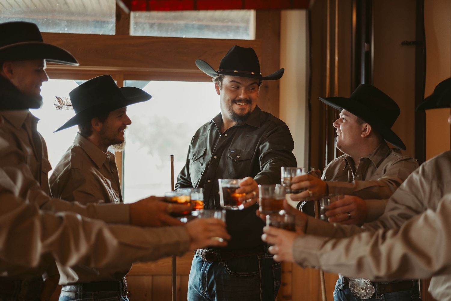 Cowboys gathered around wooden tables in a rustic restaurant setting with warm lighting. Wedding photographer DFW