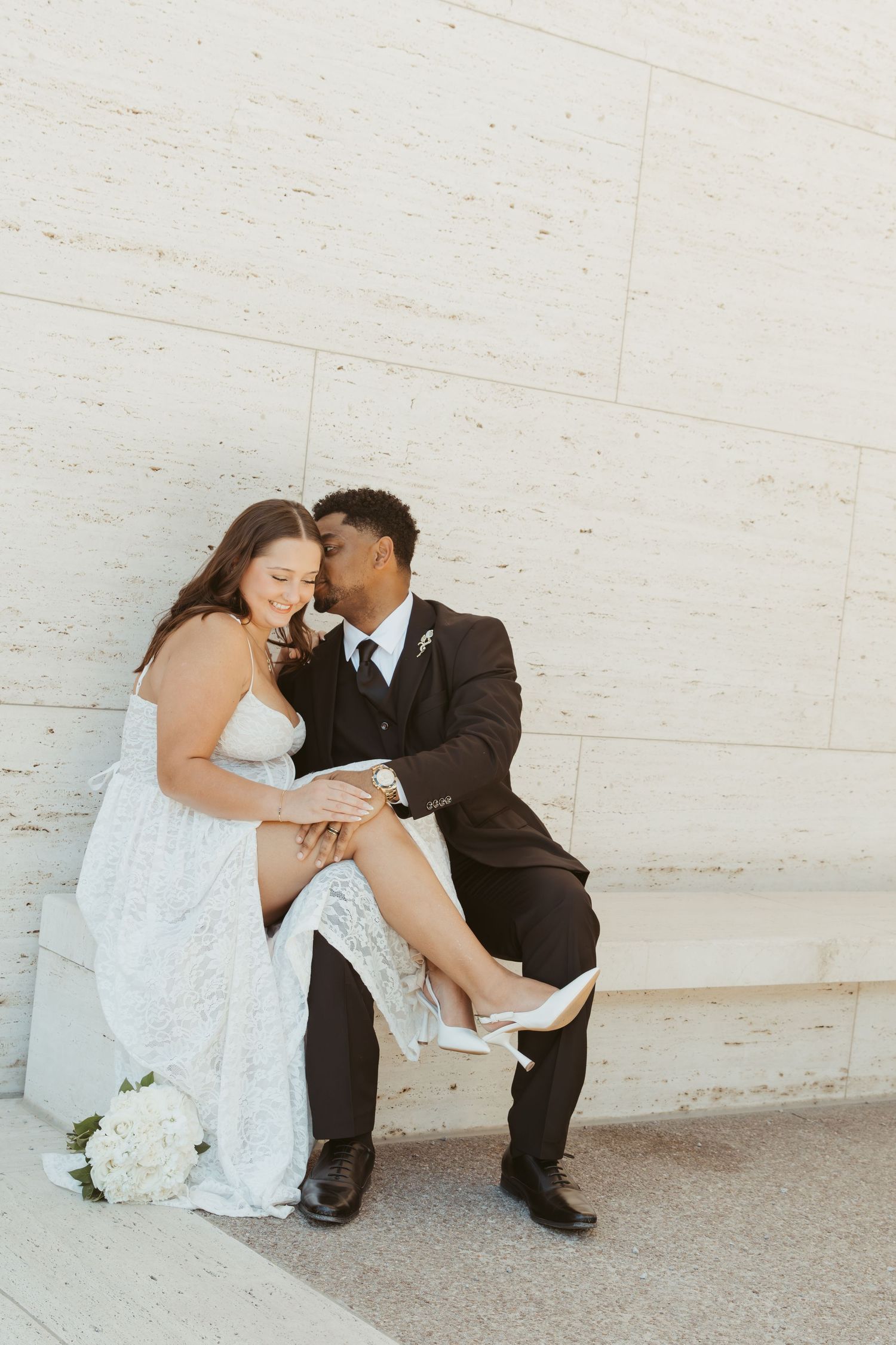 A romantic wedding couple sits and shares an intimate moment against a white wall. Wedding Photographer DFW