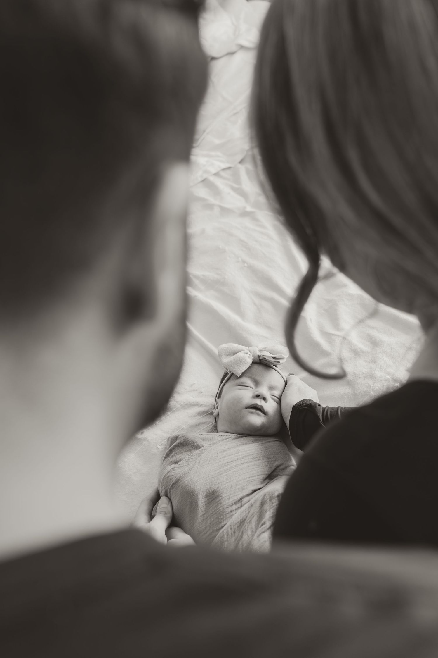 Black and white photo of newborn baby sleeping peacefully while parents gaze lovingly from above.
