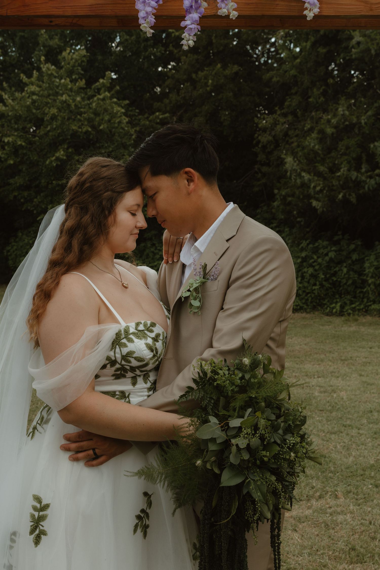 A romantic moment shared between a couple in formal attire under flowering branches in a garden setting.