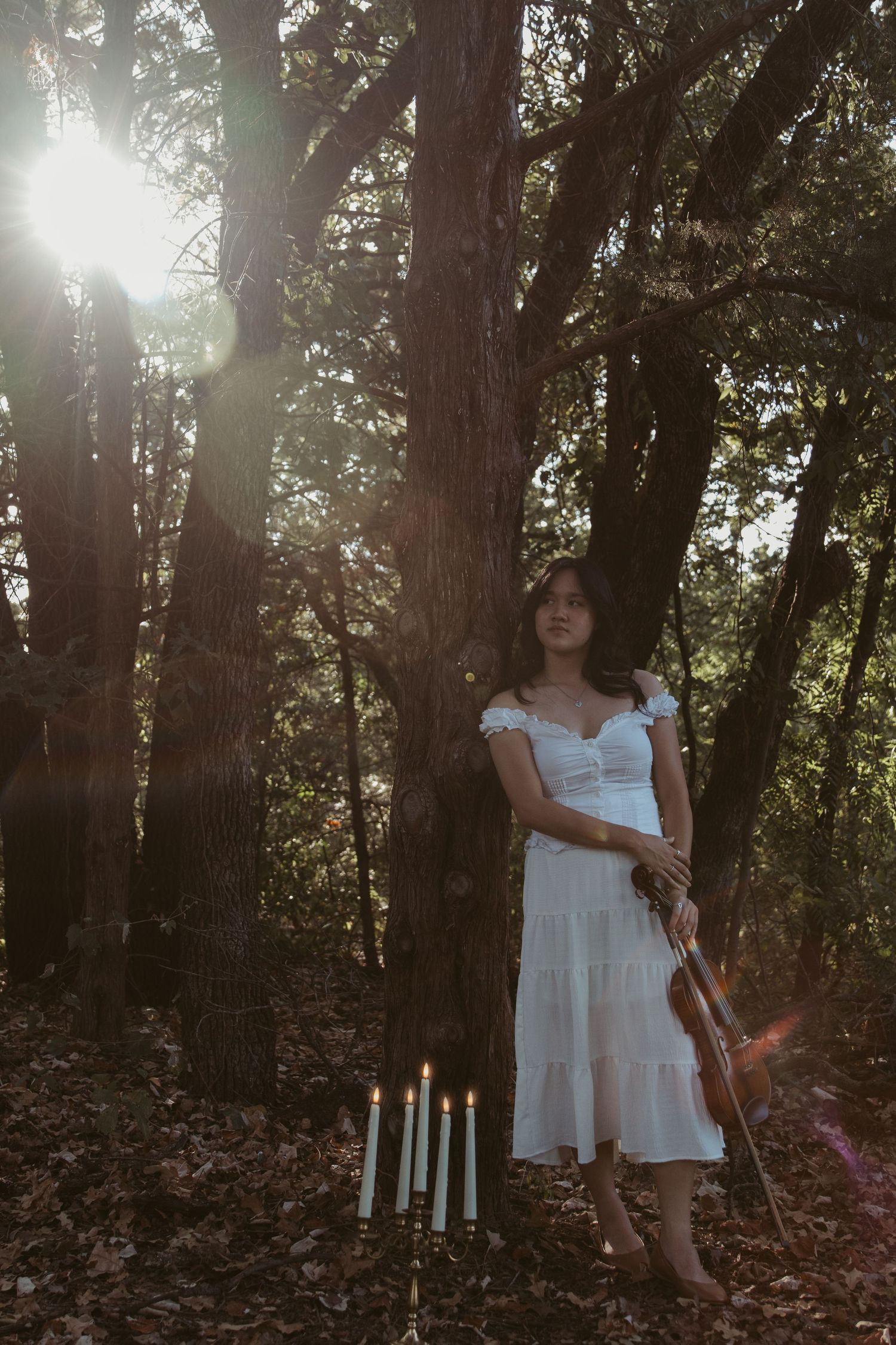 Ethereal forest scene with white candles and a violin against sunlit trees.
