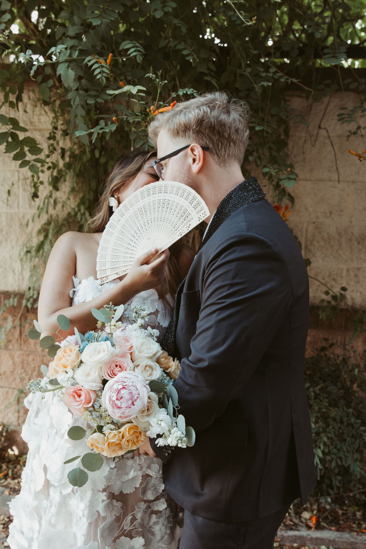 A couple shares intimate moments during their wedding photoshoot while holding a decorative white fan.