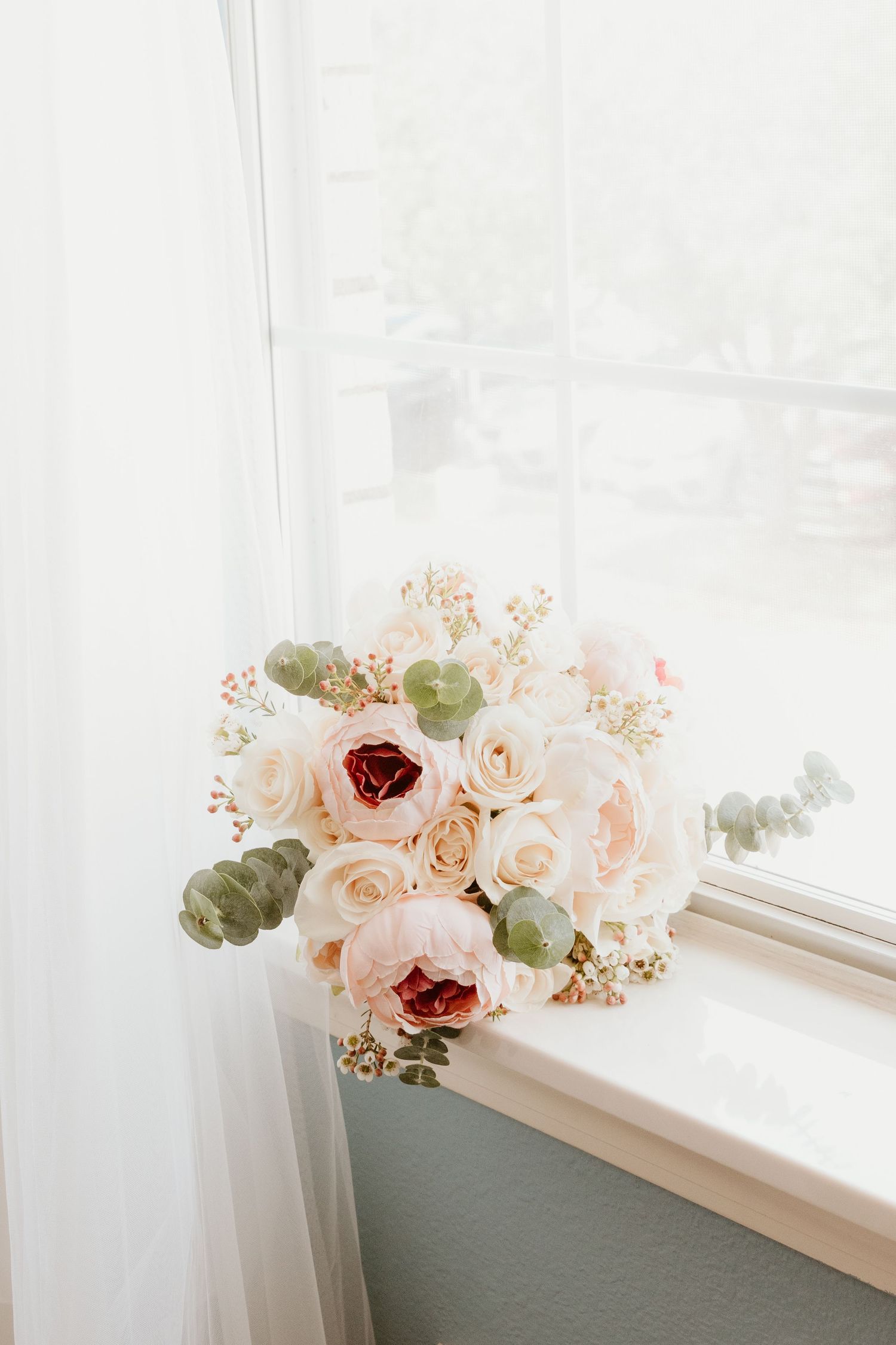 An elegant bridal bouquet of blush roses and eucalyptus leaves on a windowsill.