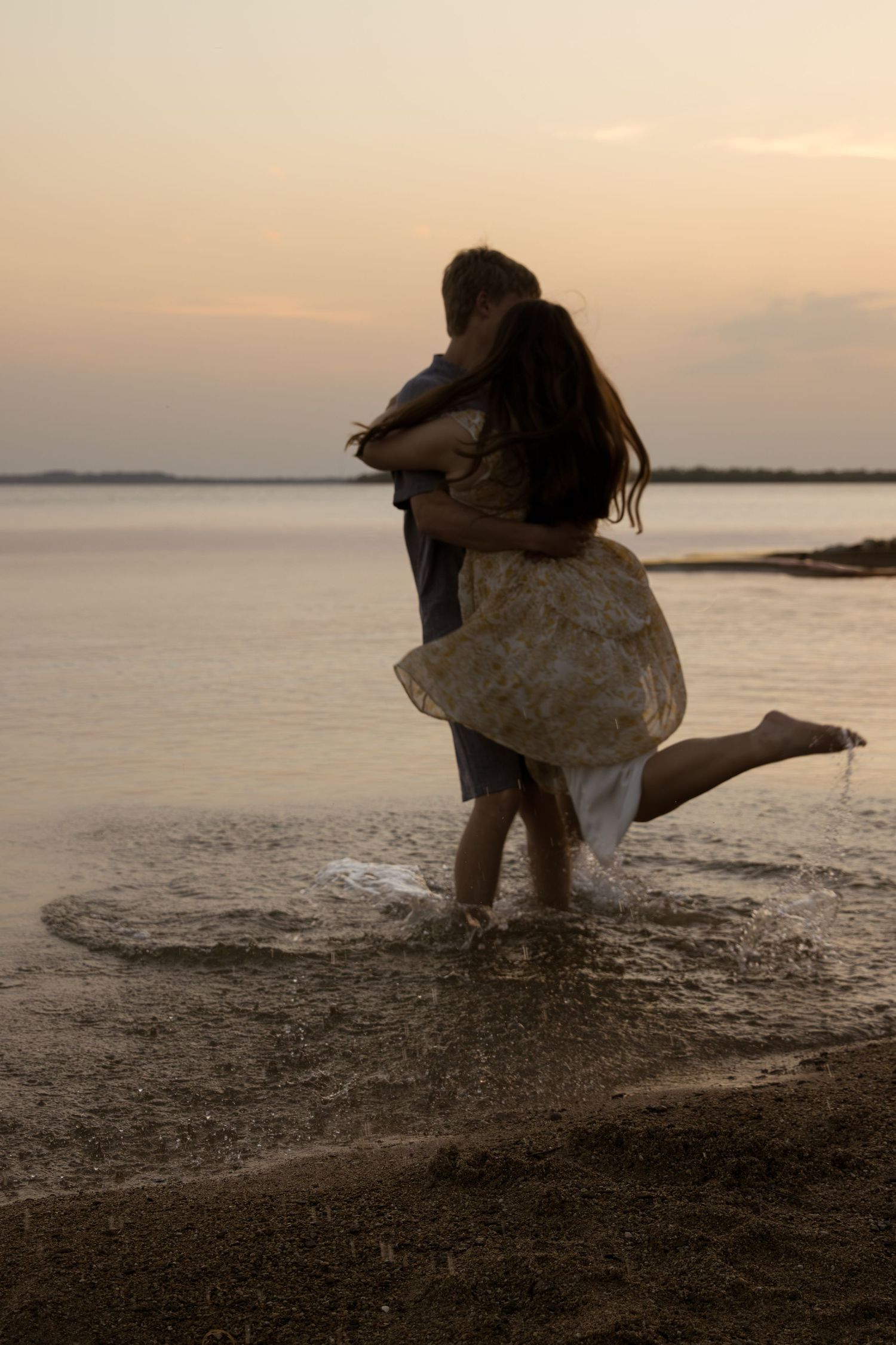 A romantic silhouette of a couple embracing on a beach during golden hour sunset with water in the background.
