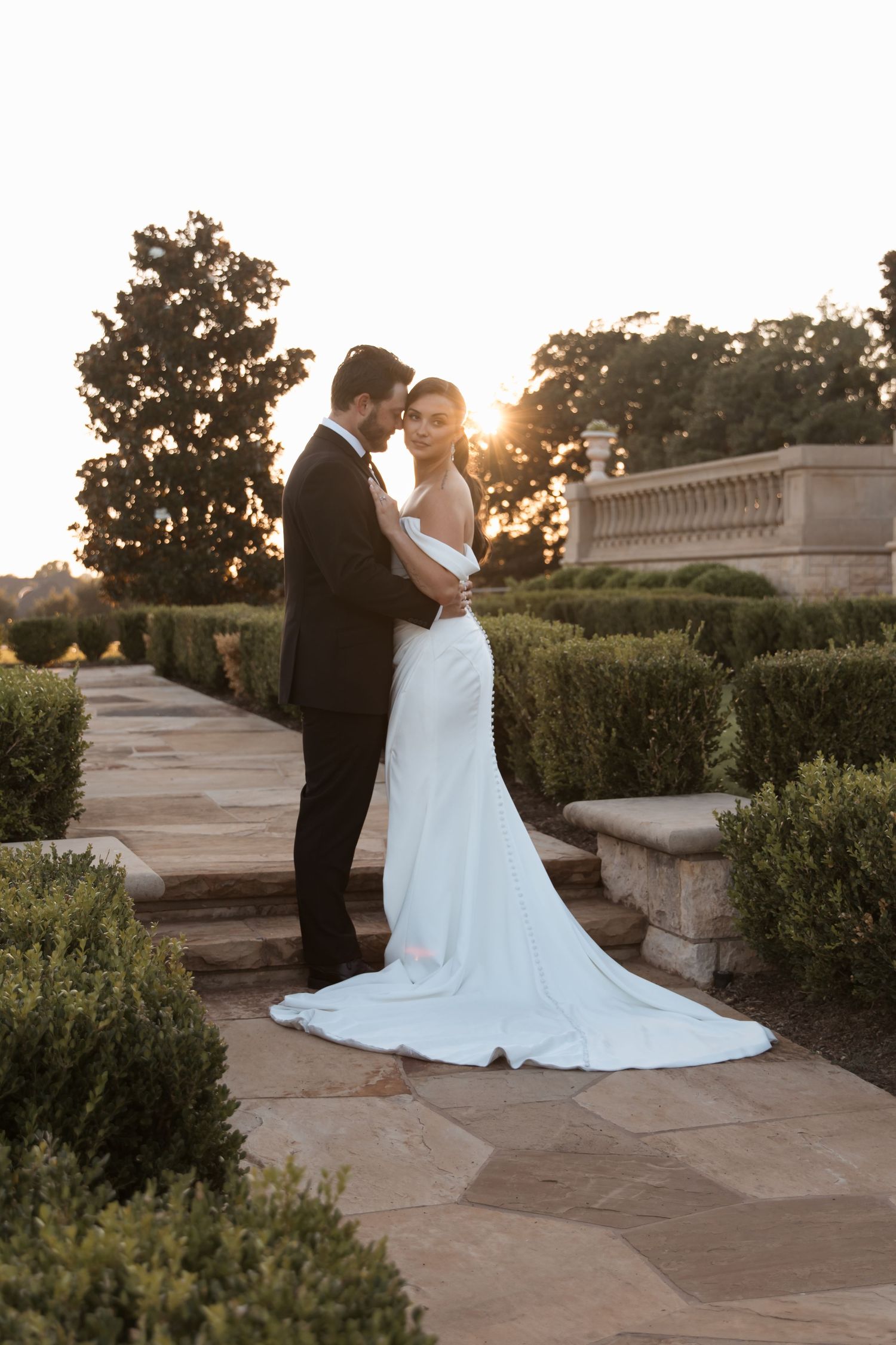 Romantic sunset wedding portrait of couple on stone terrace with trailing bridal gown.