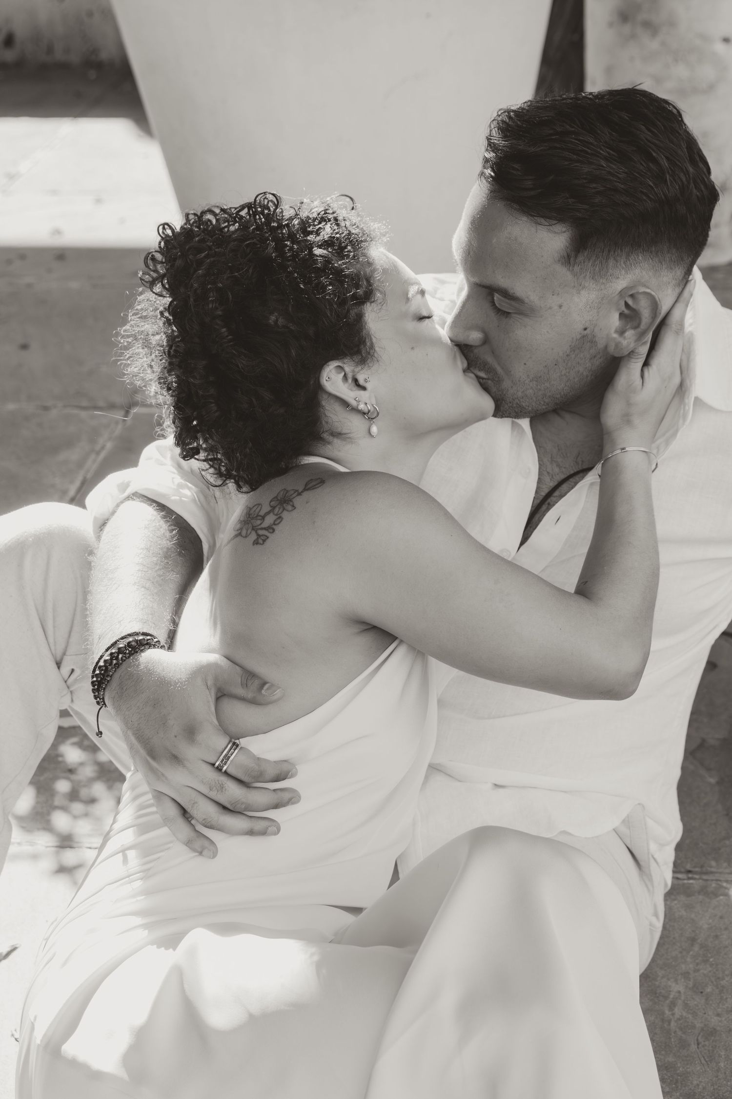 Black and white photo series showing a romantic couple embracing and kissing in casual white outfits outdoors.