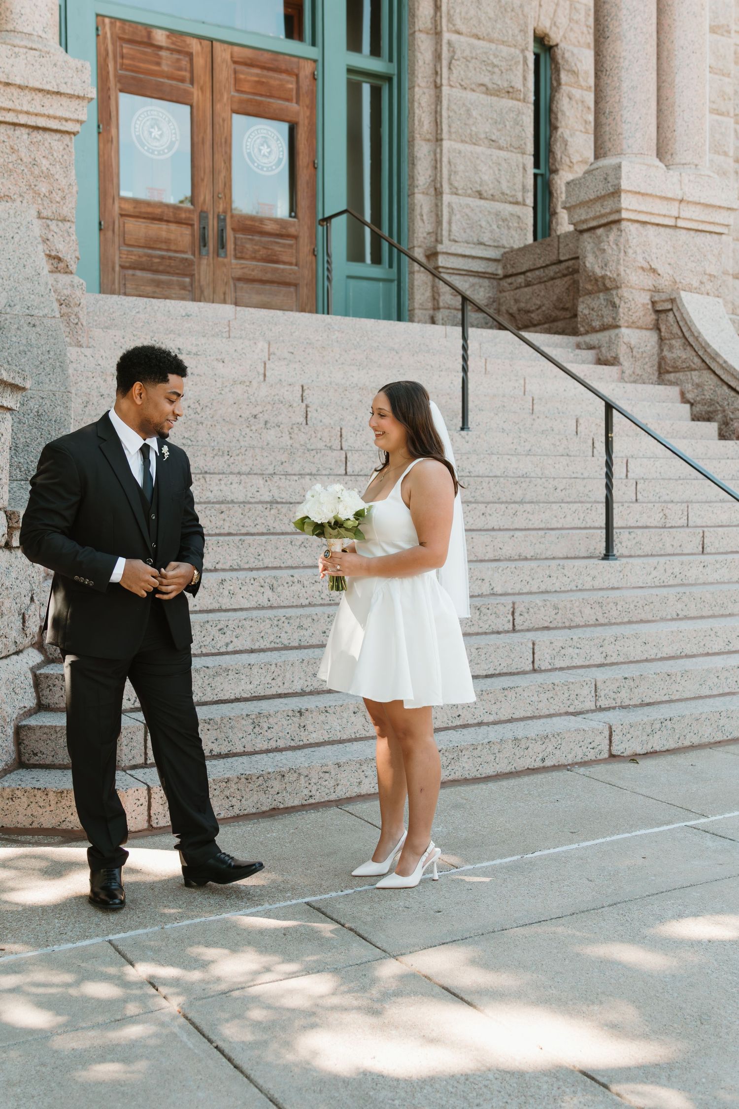 Couple shares a playful moment on stone steps of a building in formal attire. Wedding Photographer DFW