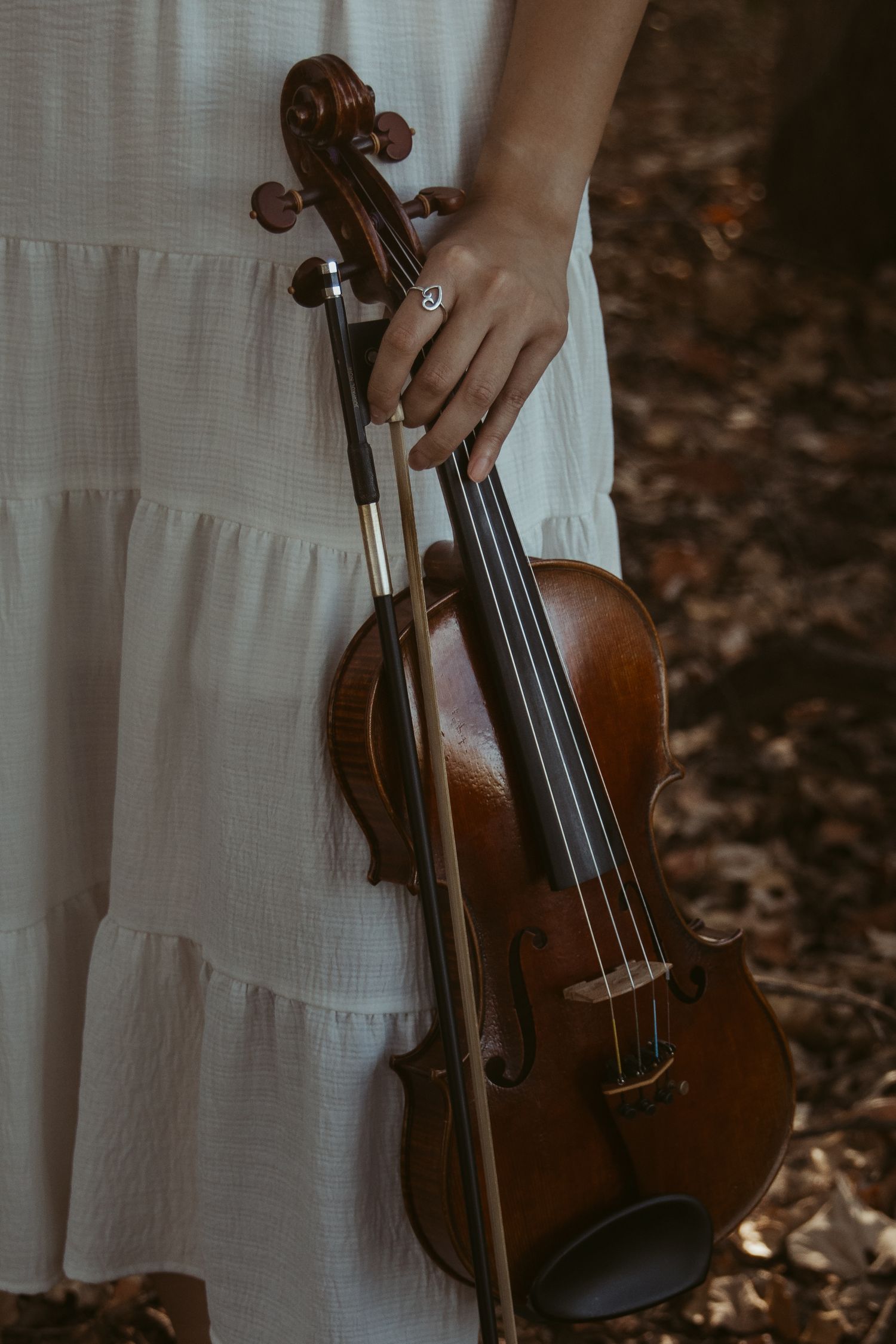 A close-up shot of hands holding a wooden violin against a white ruffled dress.