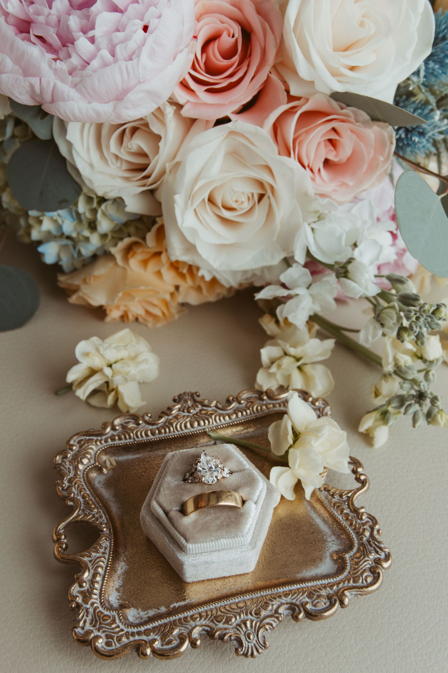 A beautiful arrangement of pink and white roses alongside an ornate silver tray holding delicate engagement rings.