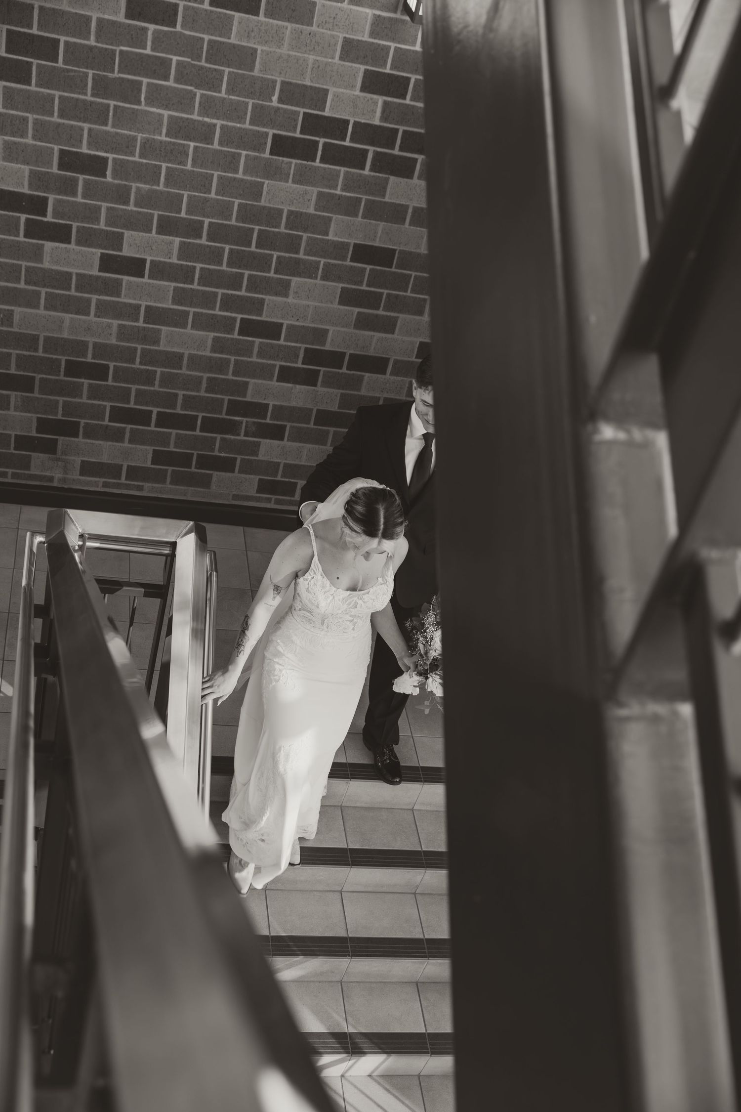 A black and white photo shows a person in white clothing walking past a brick wall with dramatic shadows.