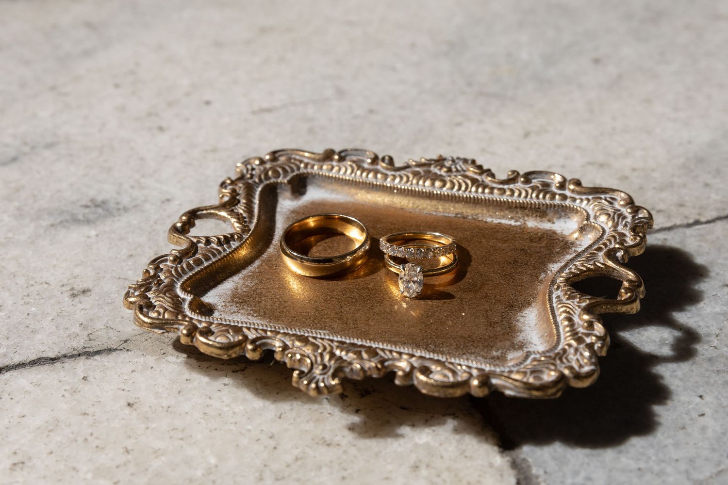 Two gold wedding rings displayed on an ornate vintage silver serving tray with decorative edges.