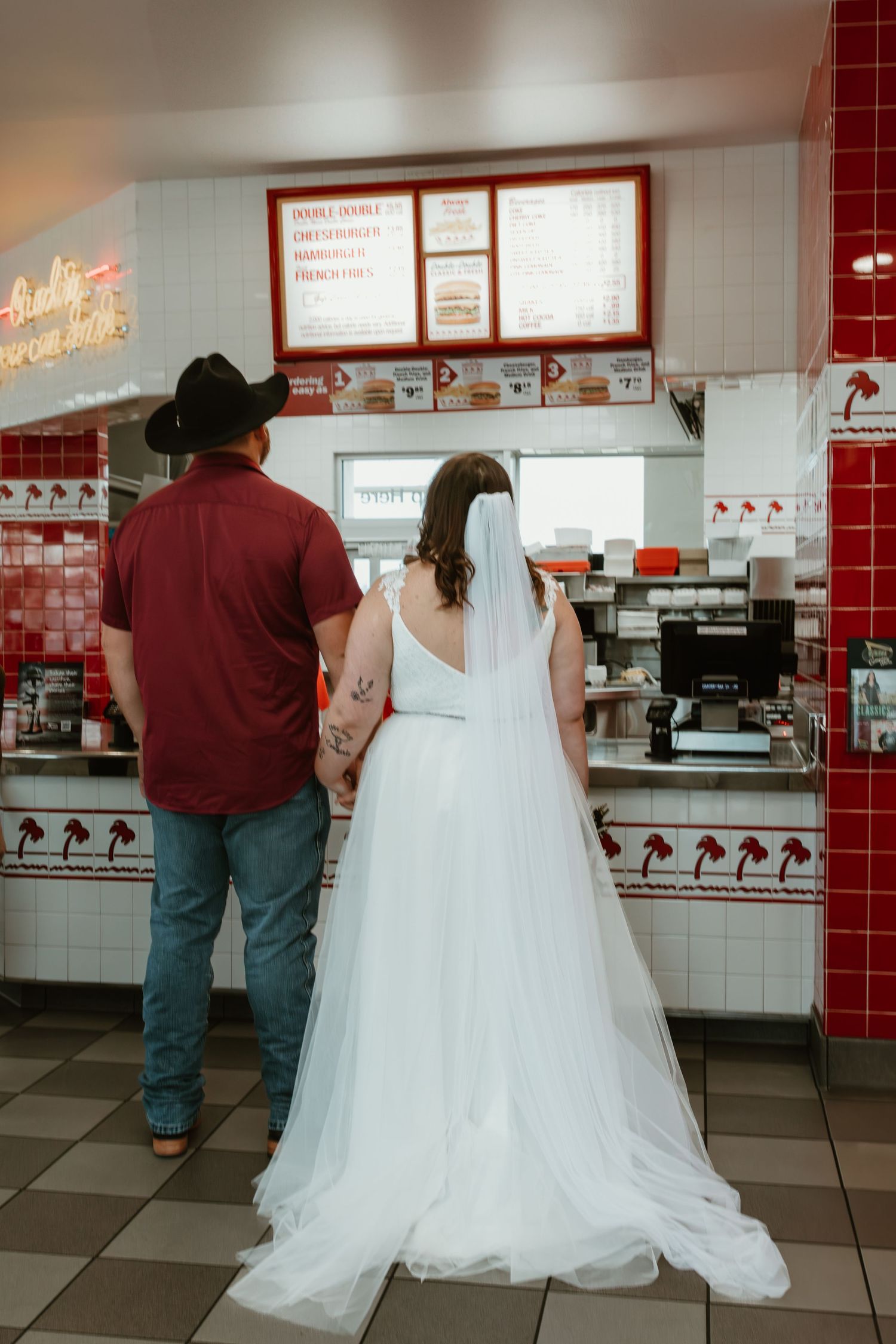 A couple in wedding attire ordering food at a diner counter with red and white tiled walls.