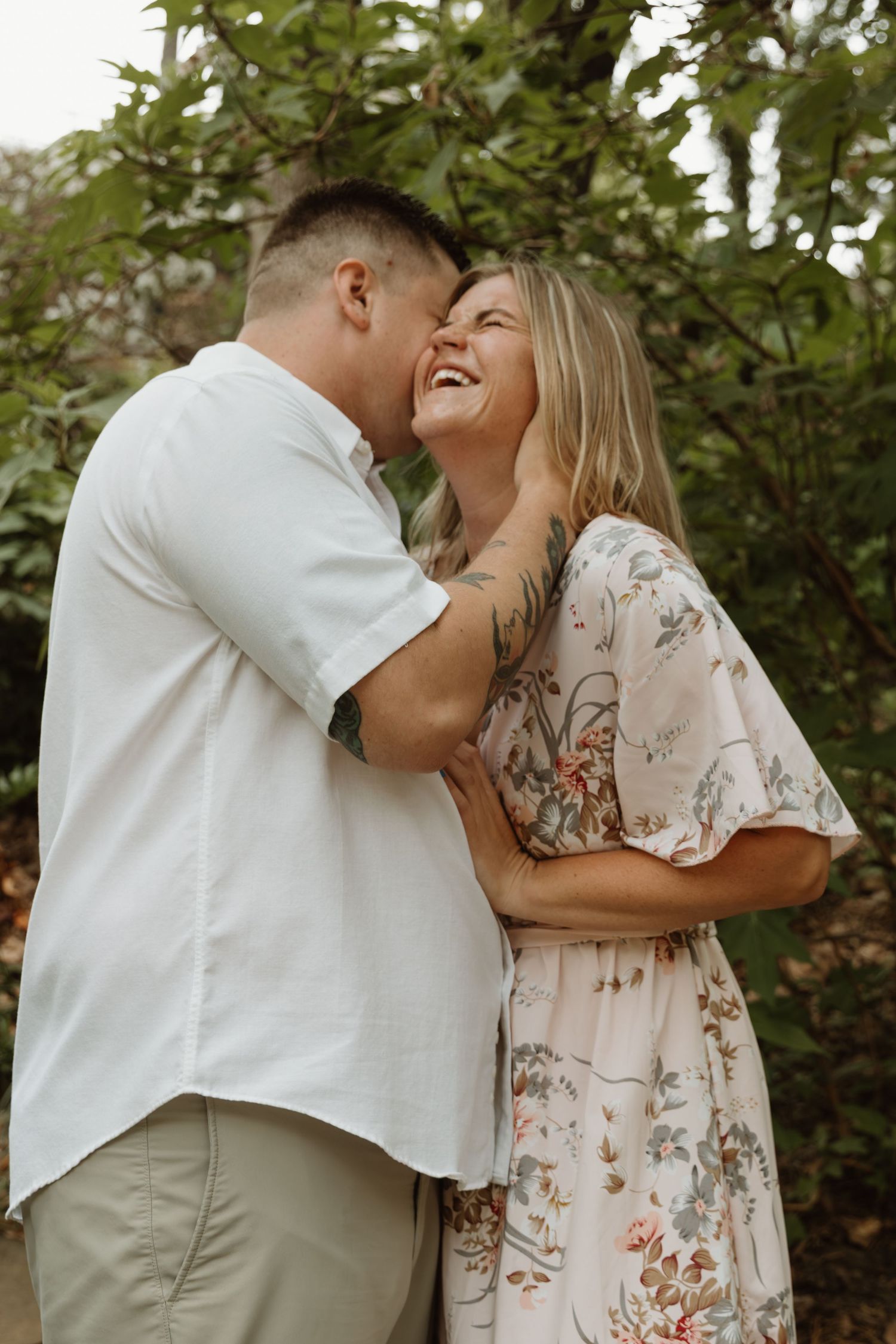 A joyful couple shares an intimate moment in a garden setting while wearing casual white and floral outfits.