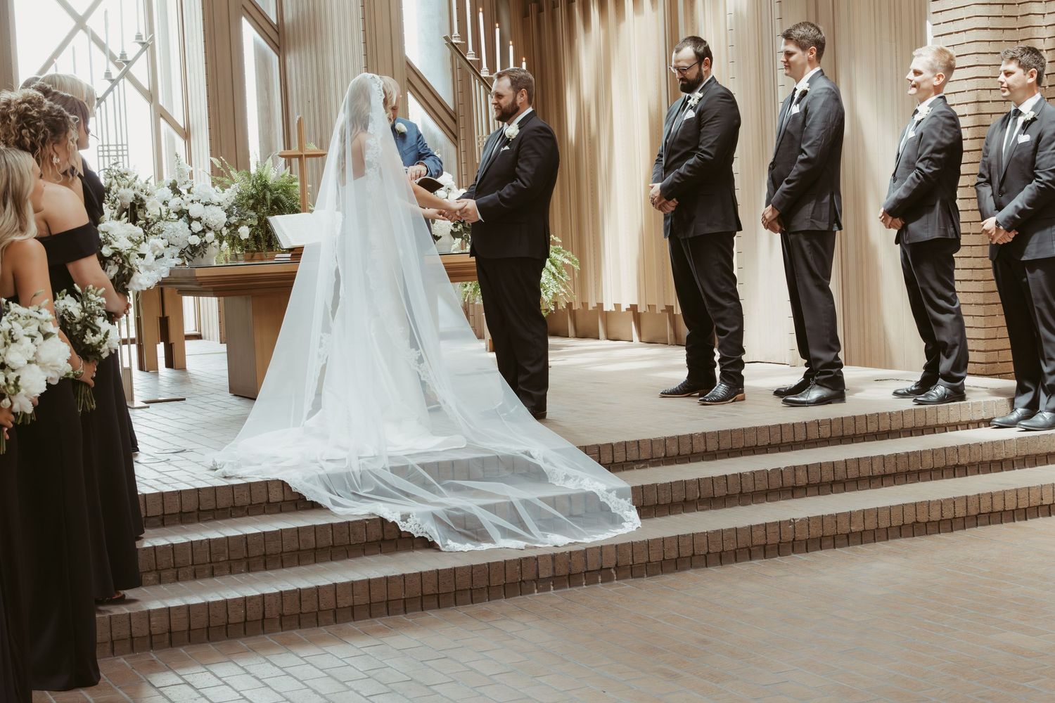 Wedding ceremony in progress at an elegant indoor venue with brick steps and flowing white curtains. Wedding Photographer DFW