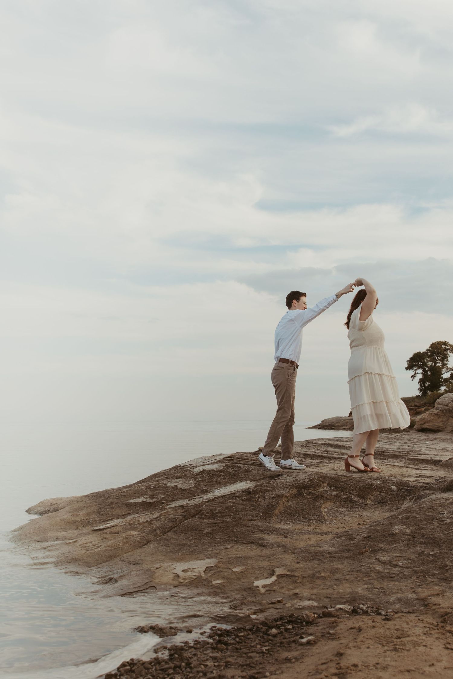A couple dances together on rocky coastal terrain against a soft cloudy sky.