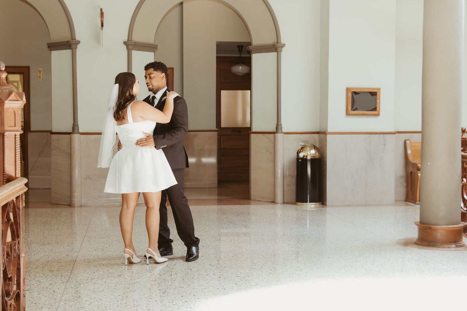 A couple dances together in an elegant white-walled hallway with arched doorways. Wedding Photographer DFW