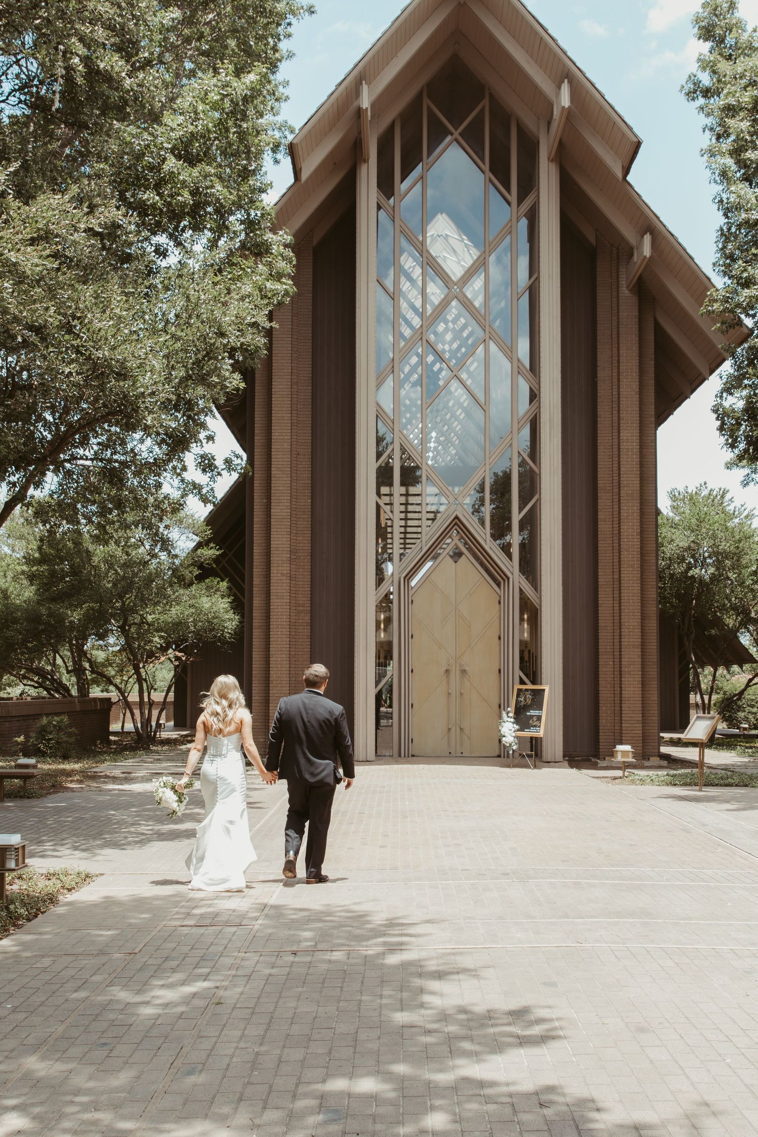 Elegant glass and wooden chapel with dramatic architectural lines and tall windows surrounded by trees on a sunny day.