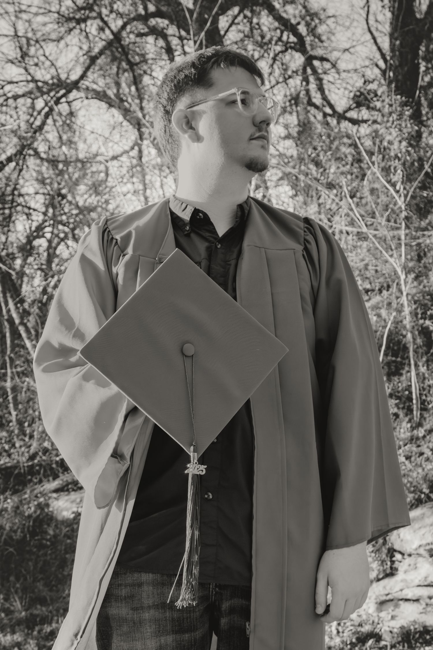 Black and white graduation portrait of graduate in cap and gown looking to the side outdoors.