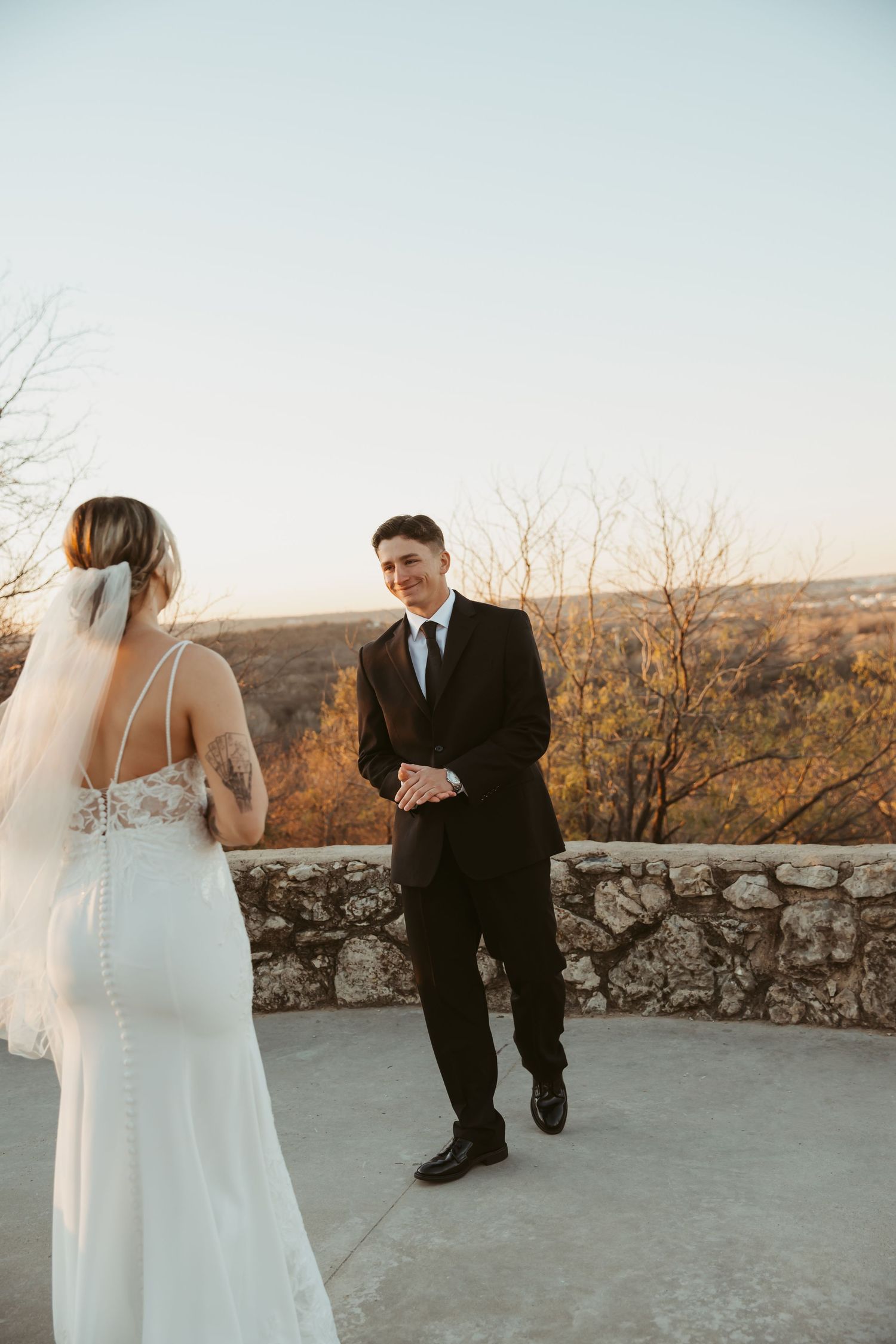 A couple in wedding attire shares an intimate moment at sunset on a stone terrace overlooking a scenic landscape.