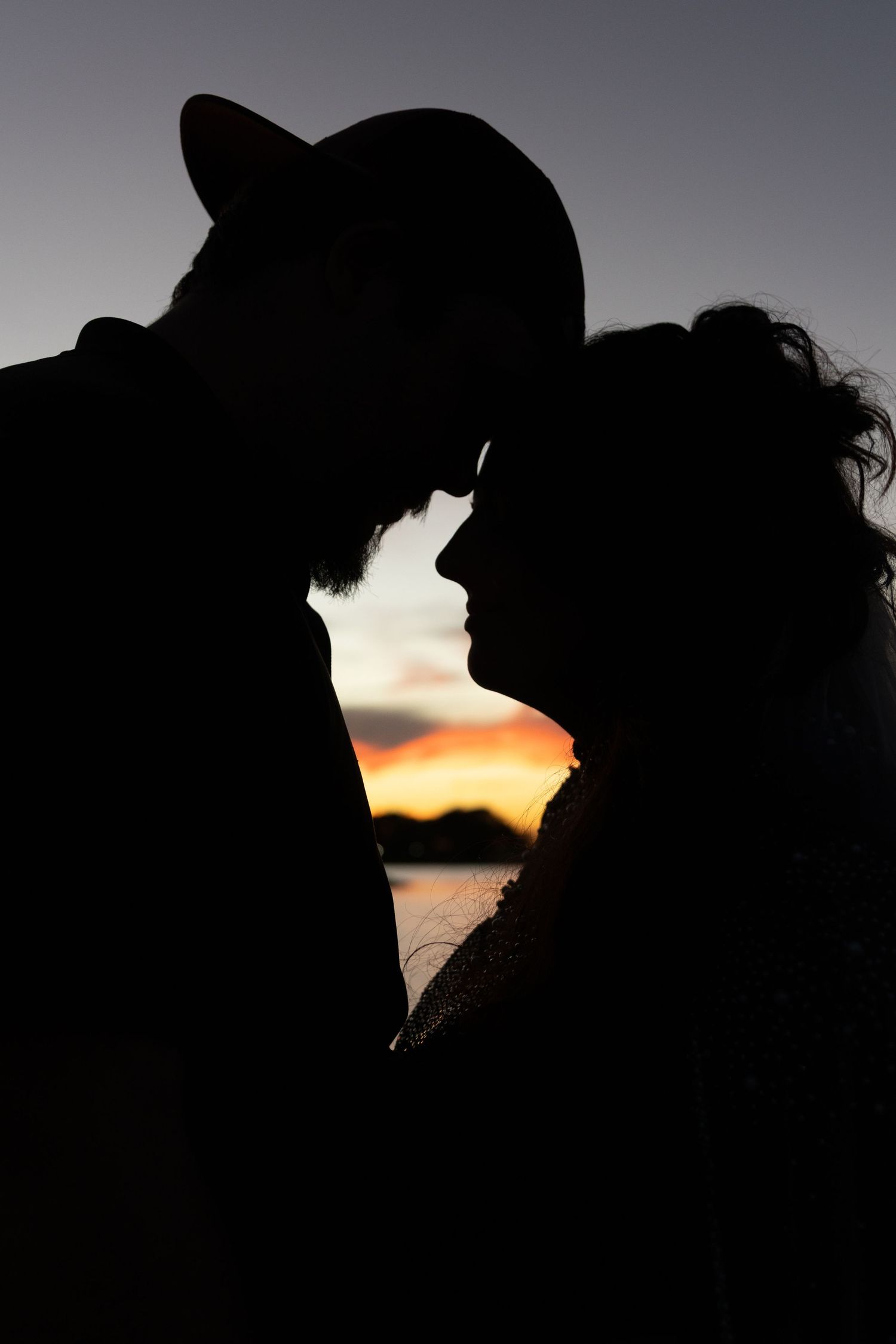 Silhouettes against a sunset sky creating a romantic seaside moment. Wedding photographer DFW