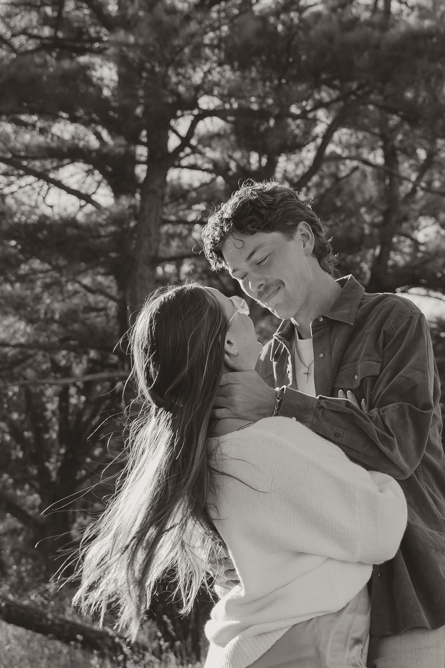 A romantic black and white photo sequence showing a couple embracing and kissing in front of pine trees.