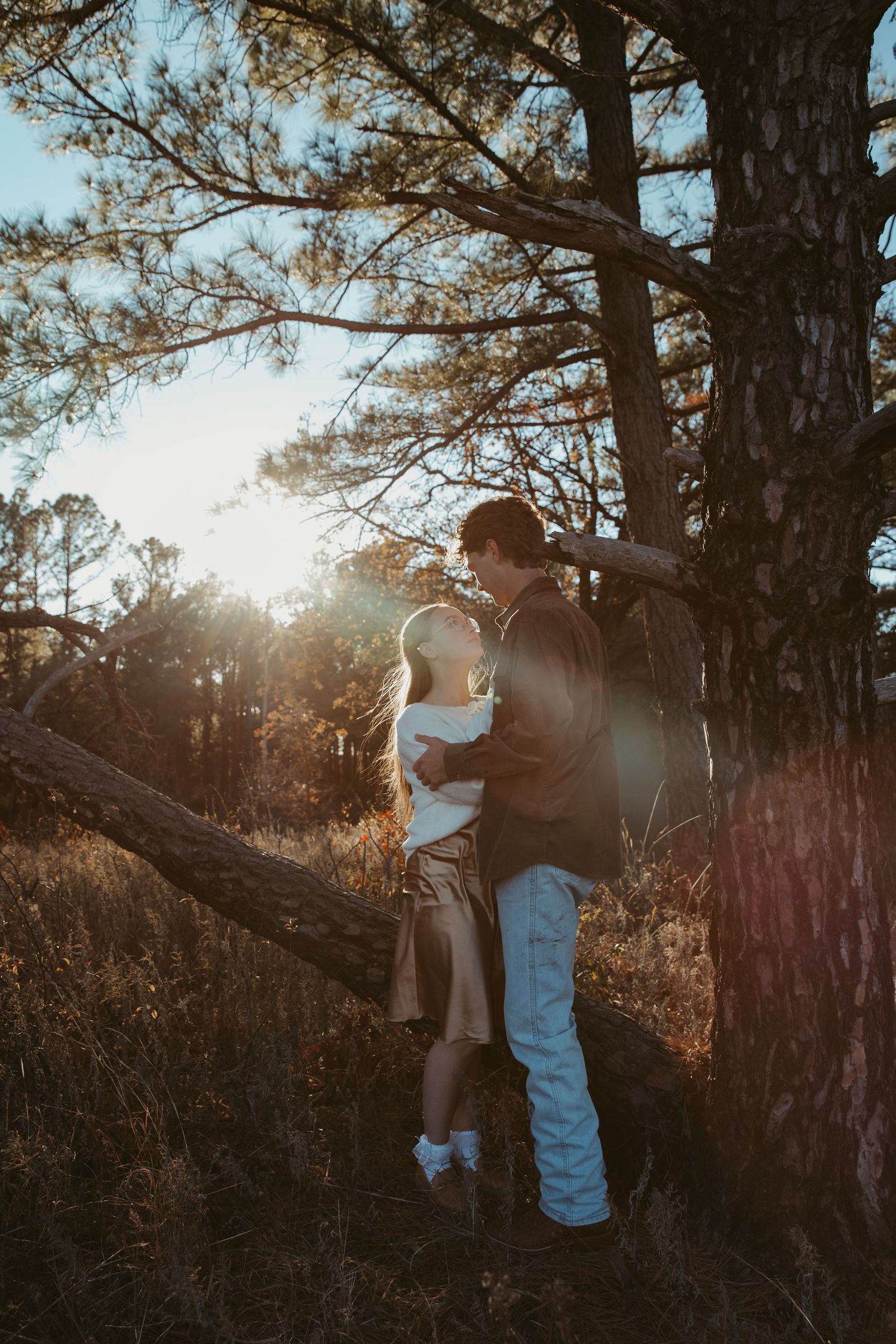 A romantic couple embraces in a sun-drenched forest setting during golden hour, creating a dreamy outdoor portrait. engagement photos DFW