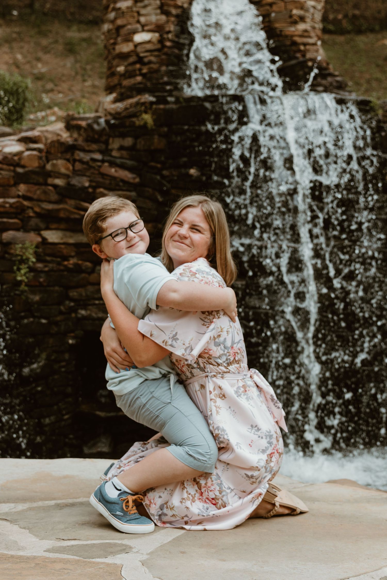 A tender embrace shared between two people in front of a cascading stone waterfall on a sunny day.