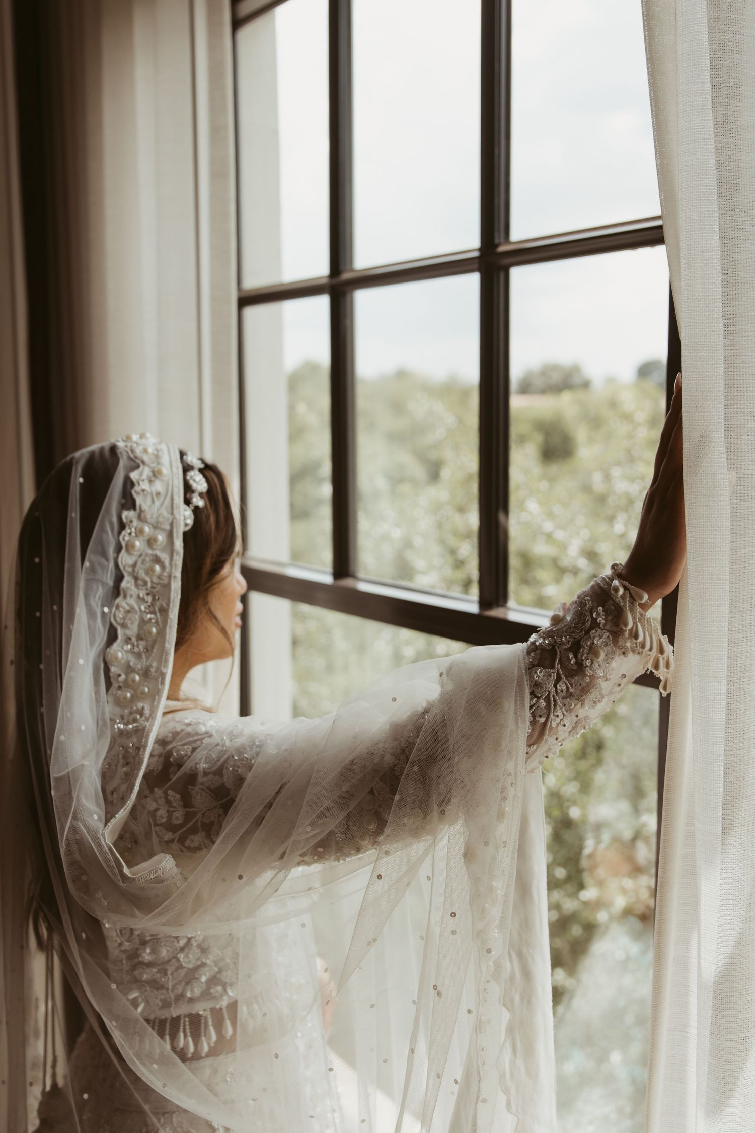 Silhouette shot showing bridal veils hanging by large windows with natural light pouring in.