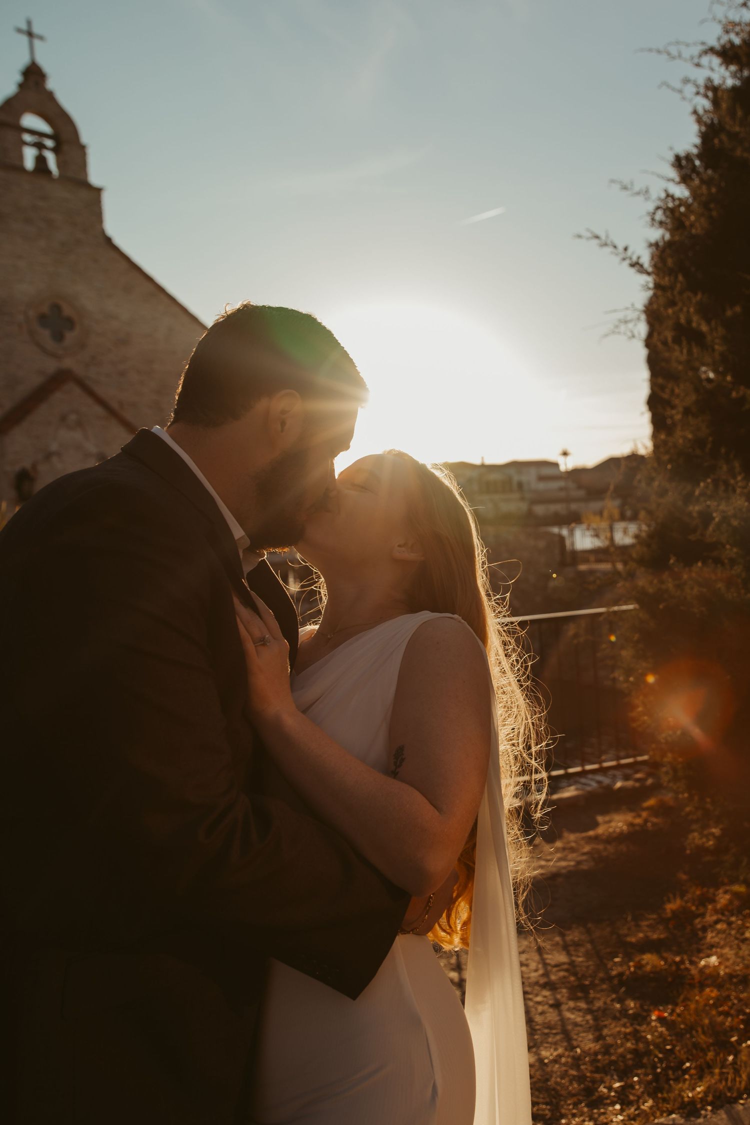 A romantic silhouette of a couple embracing at sunset with a church steeple in the background.