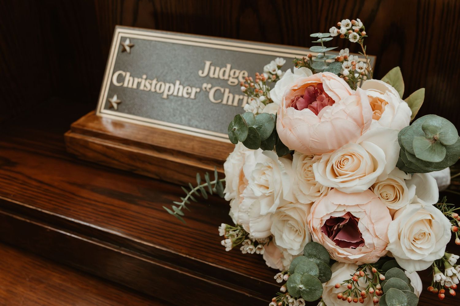 A floral wedding bouquet with pink and white roses placed next to a judge's nameplate.