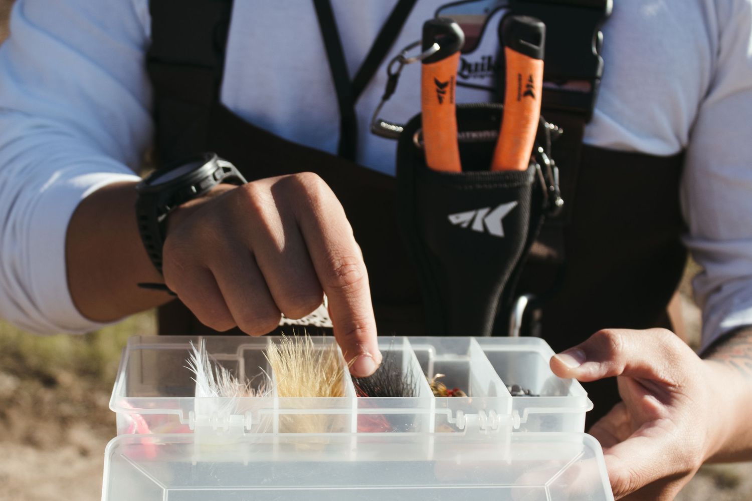 Close-up of hands organizing fishing flies in a tackle box compartment.