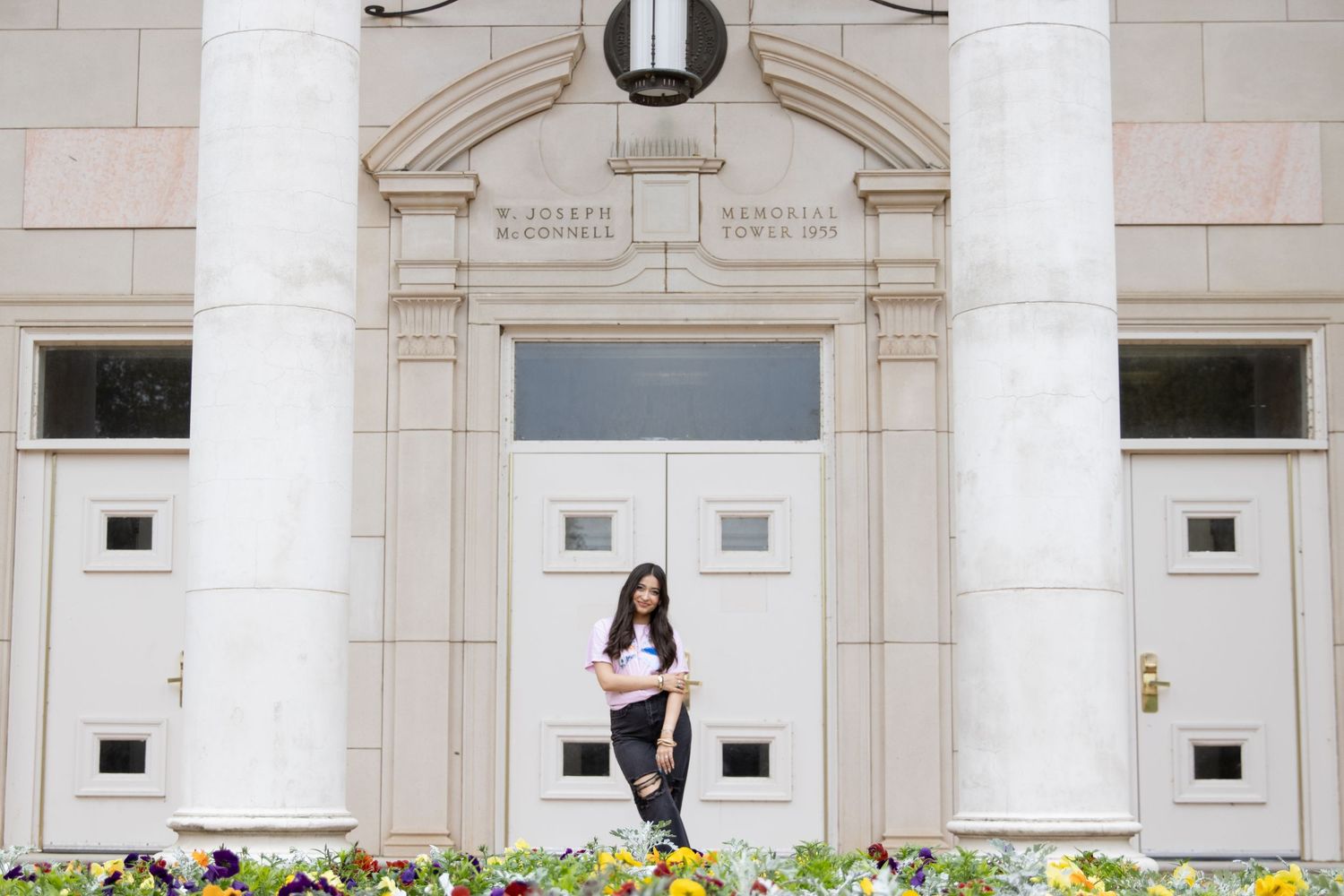 A student stands on steps in front of a grand white stone entrance with classical architectural details.