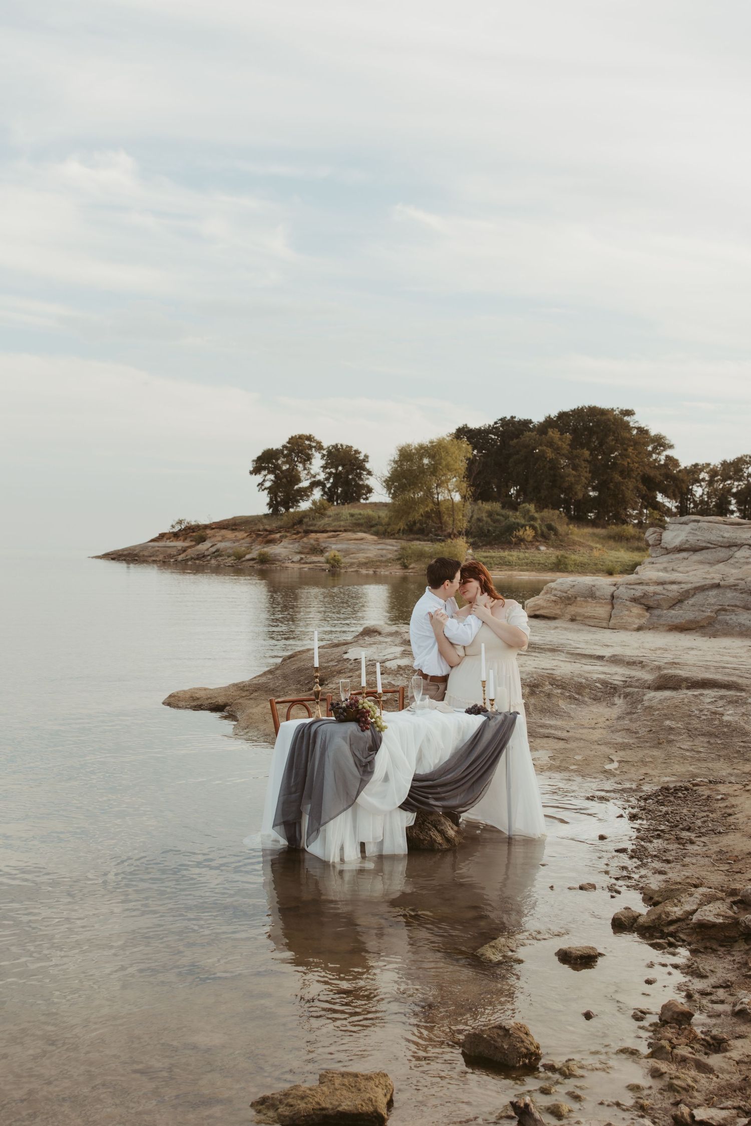 Intimate waterfront scene with decorated table and couple on rocky coastline.