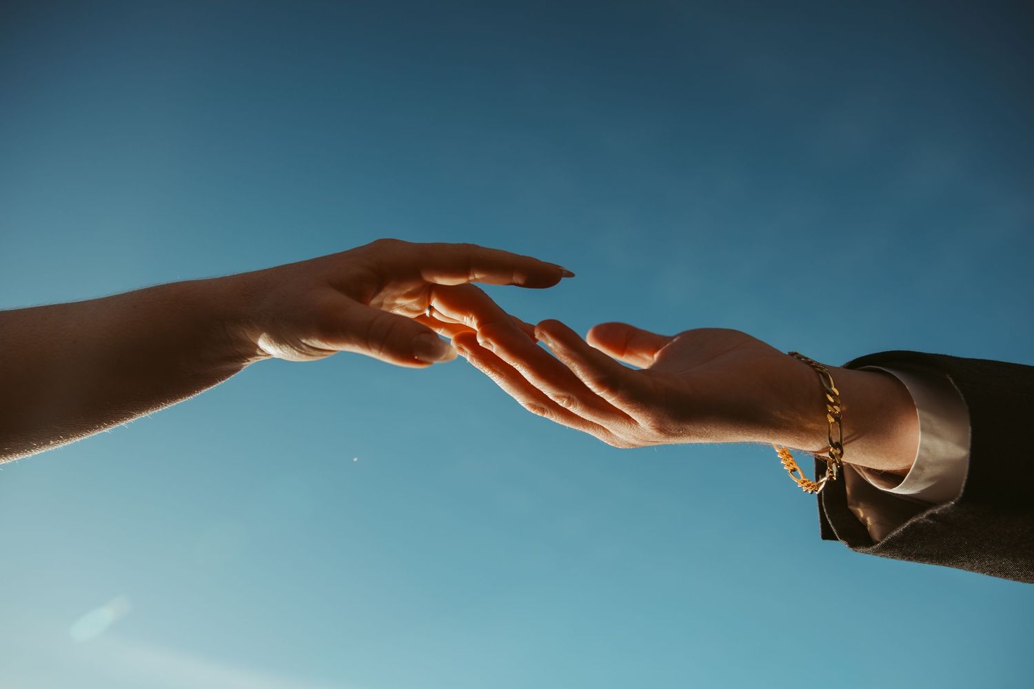 Two hands reach toward each other against a blue sky background in a dramatic recreation of Michelangelo's Creation.