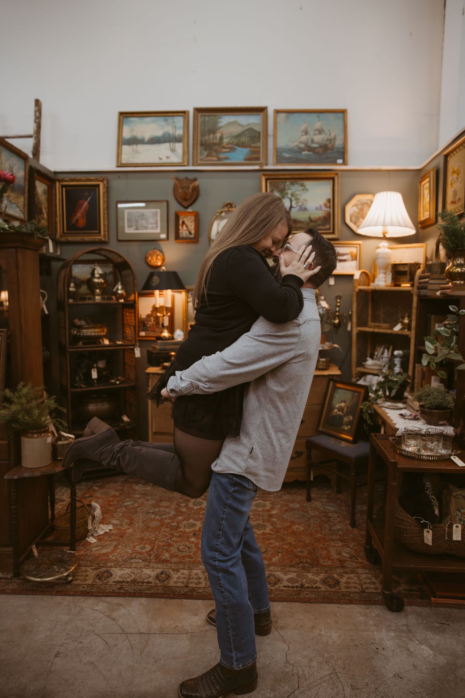 Dancing couple in casual attire enjoying a playful moment in an antique-filled room.