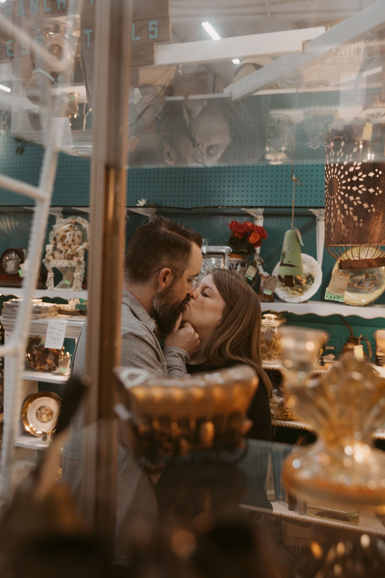 A romantic couple shares an intimate kiss in a cozy cafe setting with warm lighting and decorative details in the background.