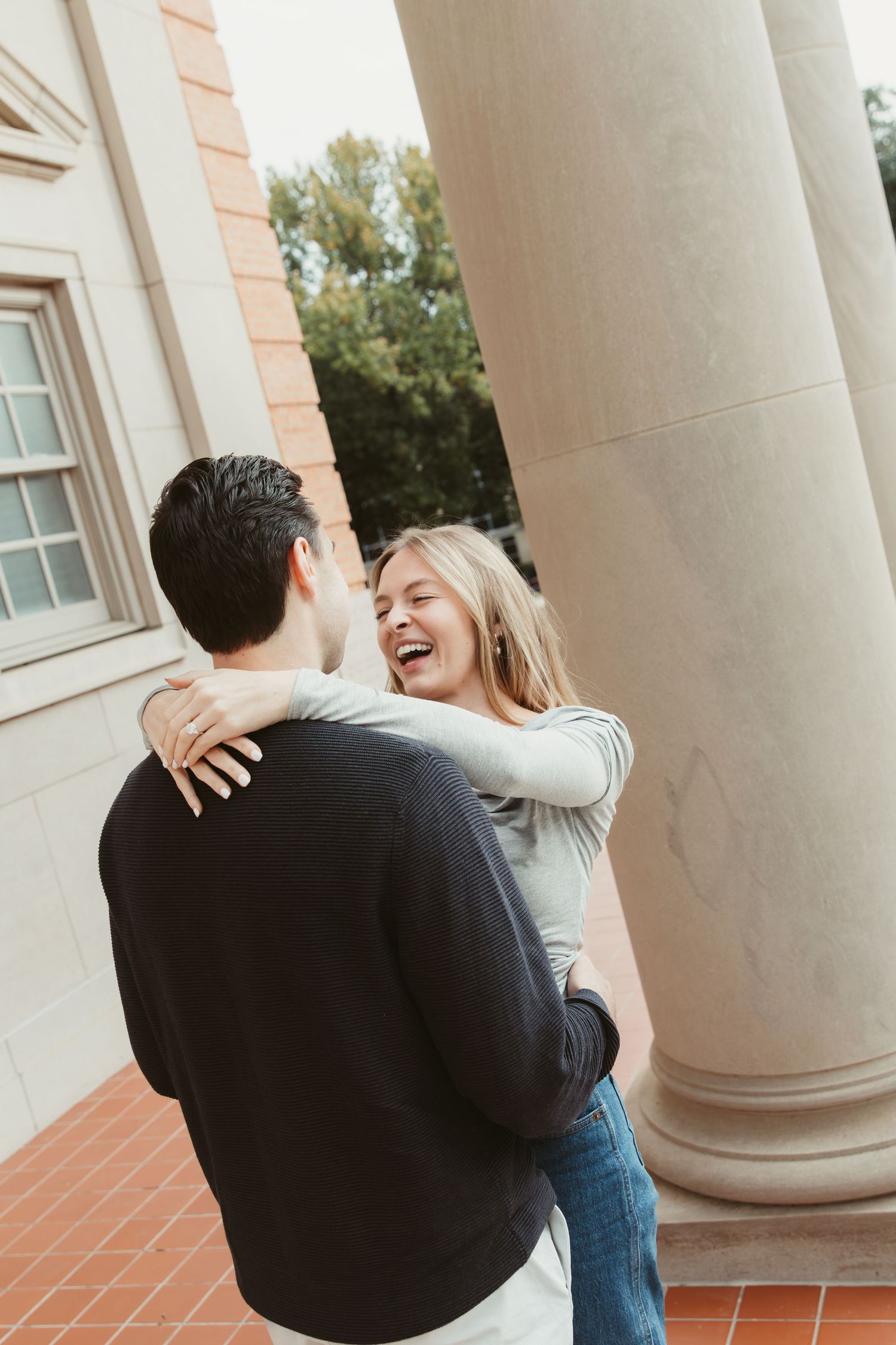 A joyful couple shares a candid laughing moment while embracing near elegant architectural columns. engagement photos Fort Worth