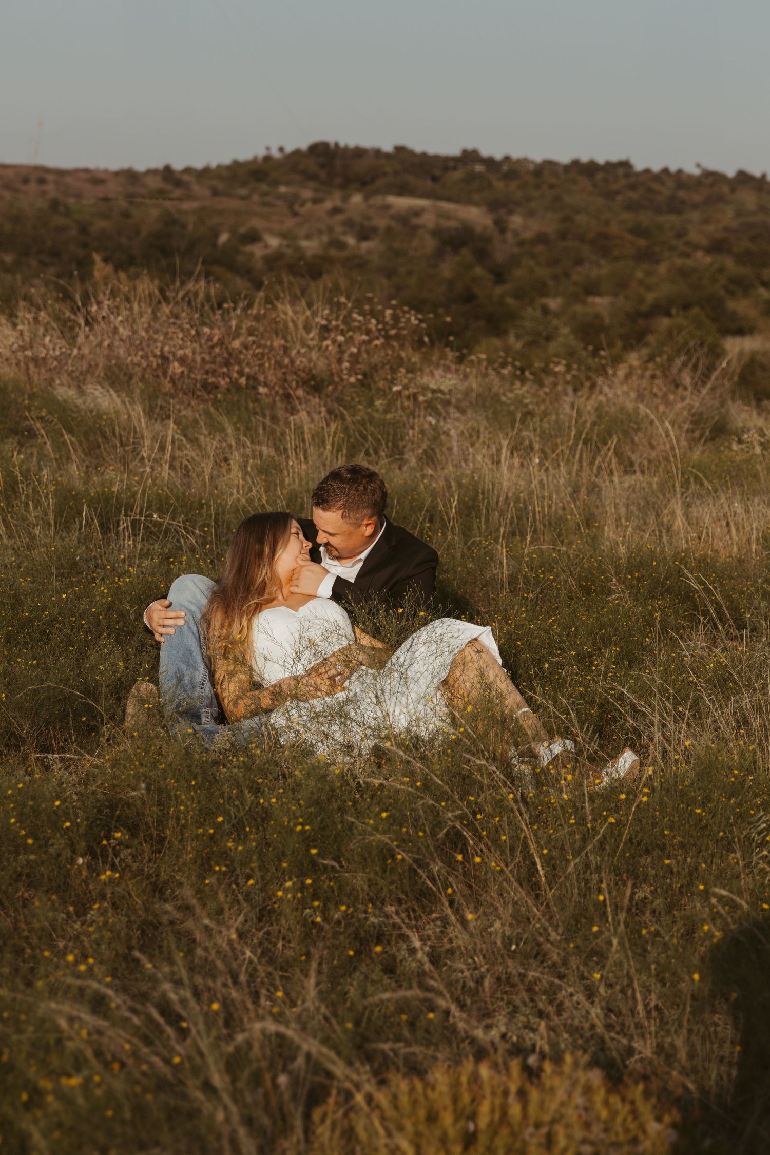 A couple embraces intimately while laying in a golden field of tall grass during sunset. Wedding Photographer DFW