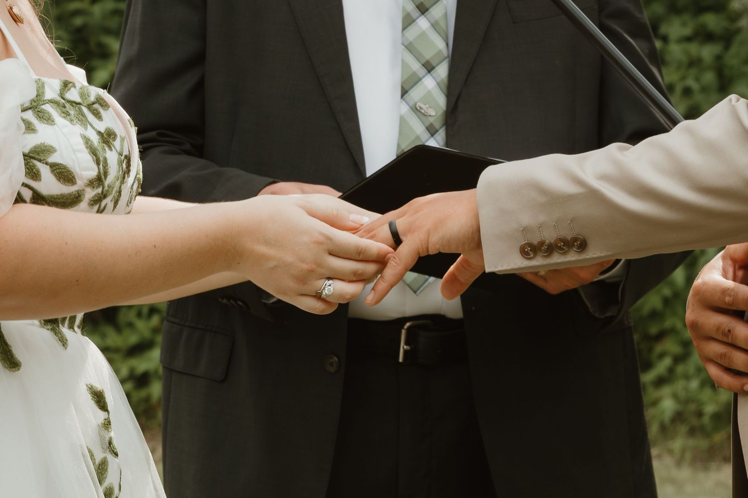Close up of hands exchanging wedding rings during an outdoor ceremony.