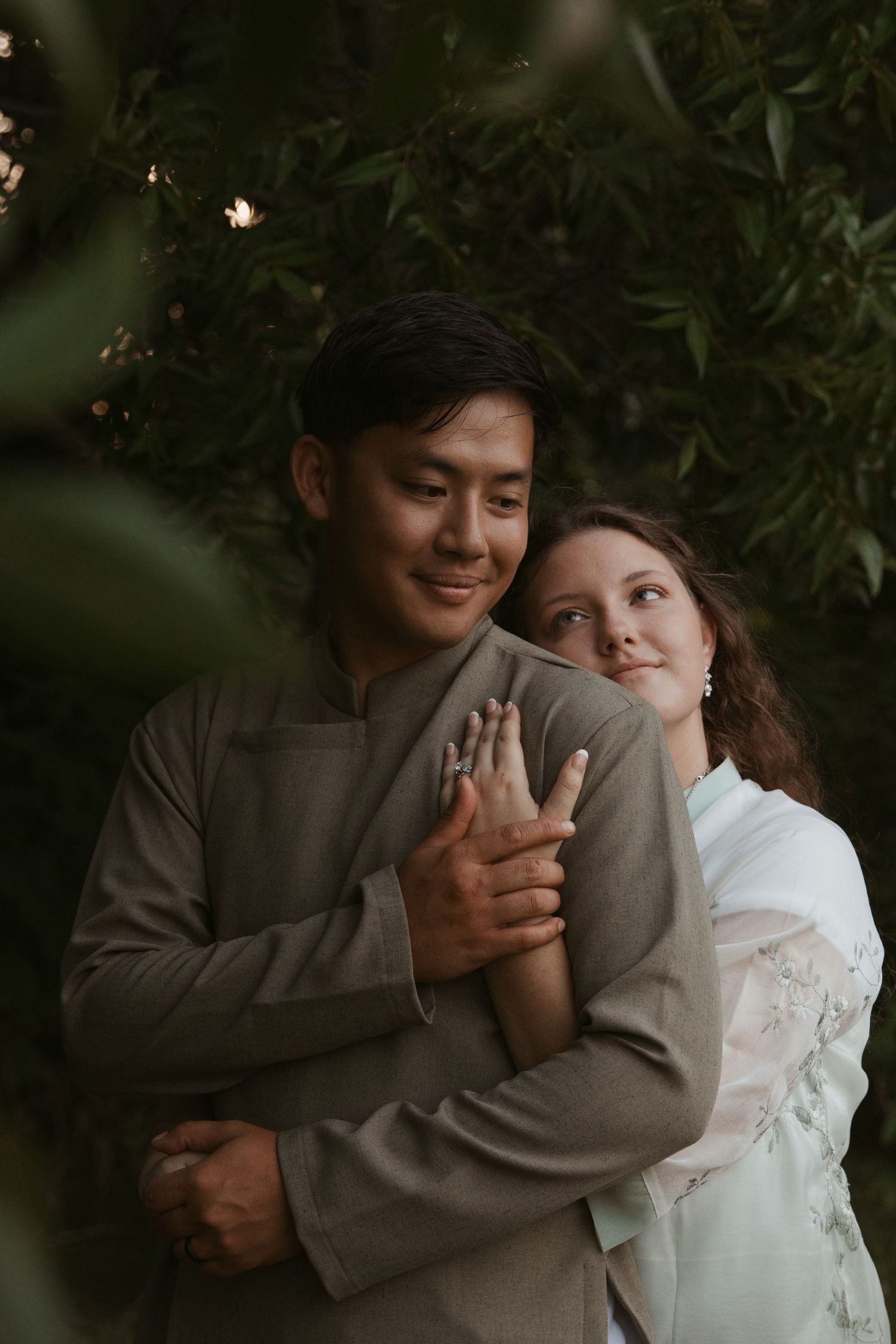 An intimate couple shares a tender moment together in a darkly lit garden setting.