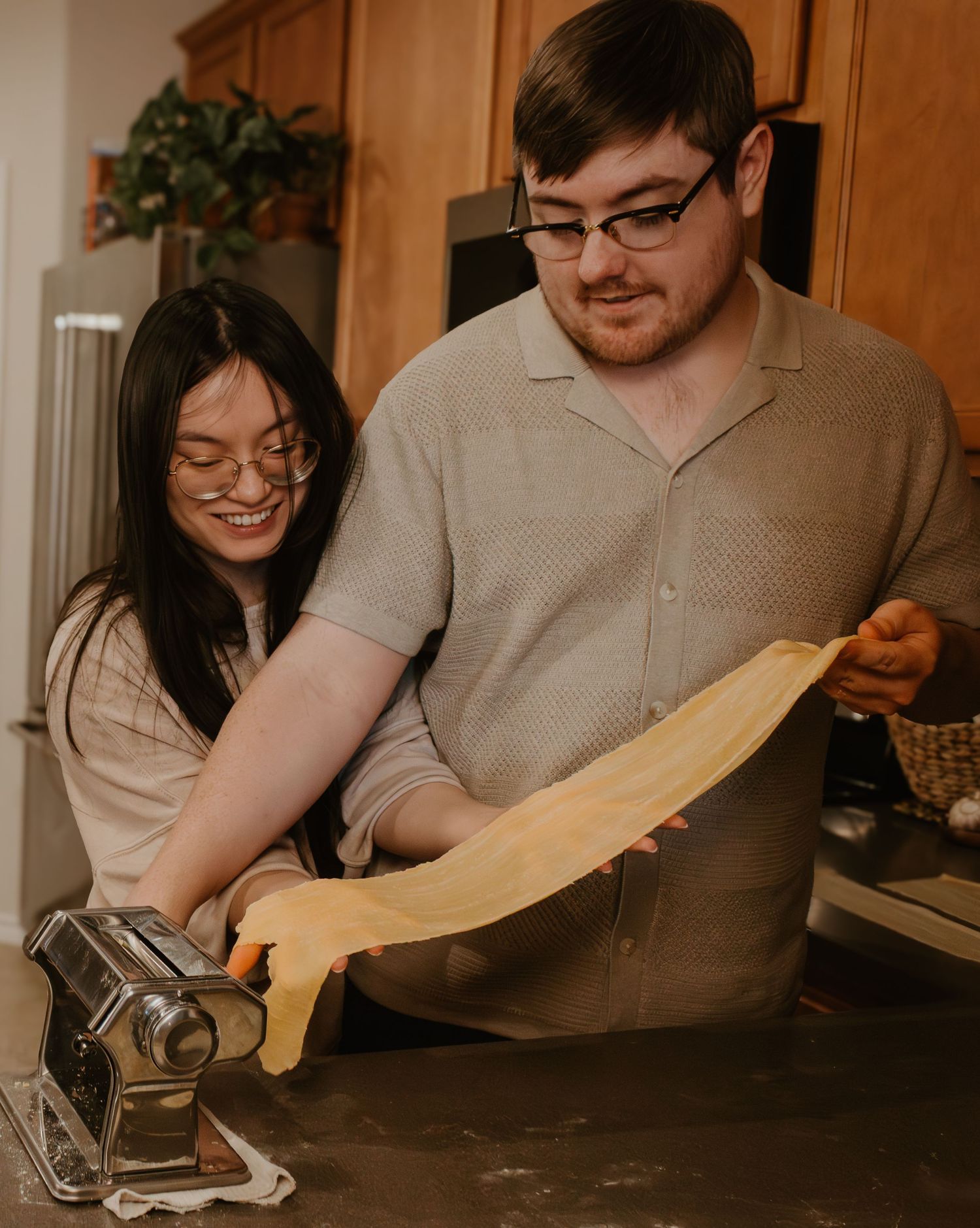 A couple using a pasta machine to roll out fresh homemade pasta dough.