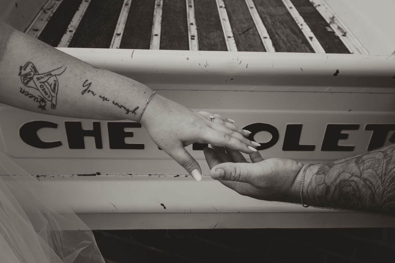 Two tattooed hands touch over a vintage Chevrolet truck bed in black and white.