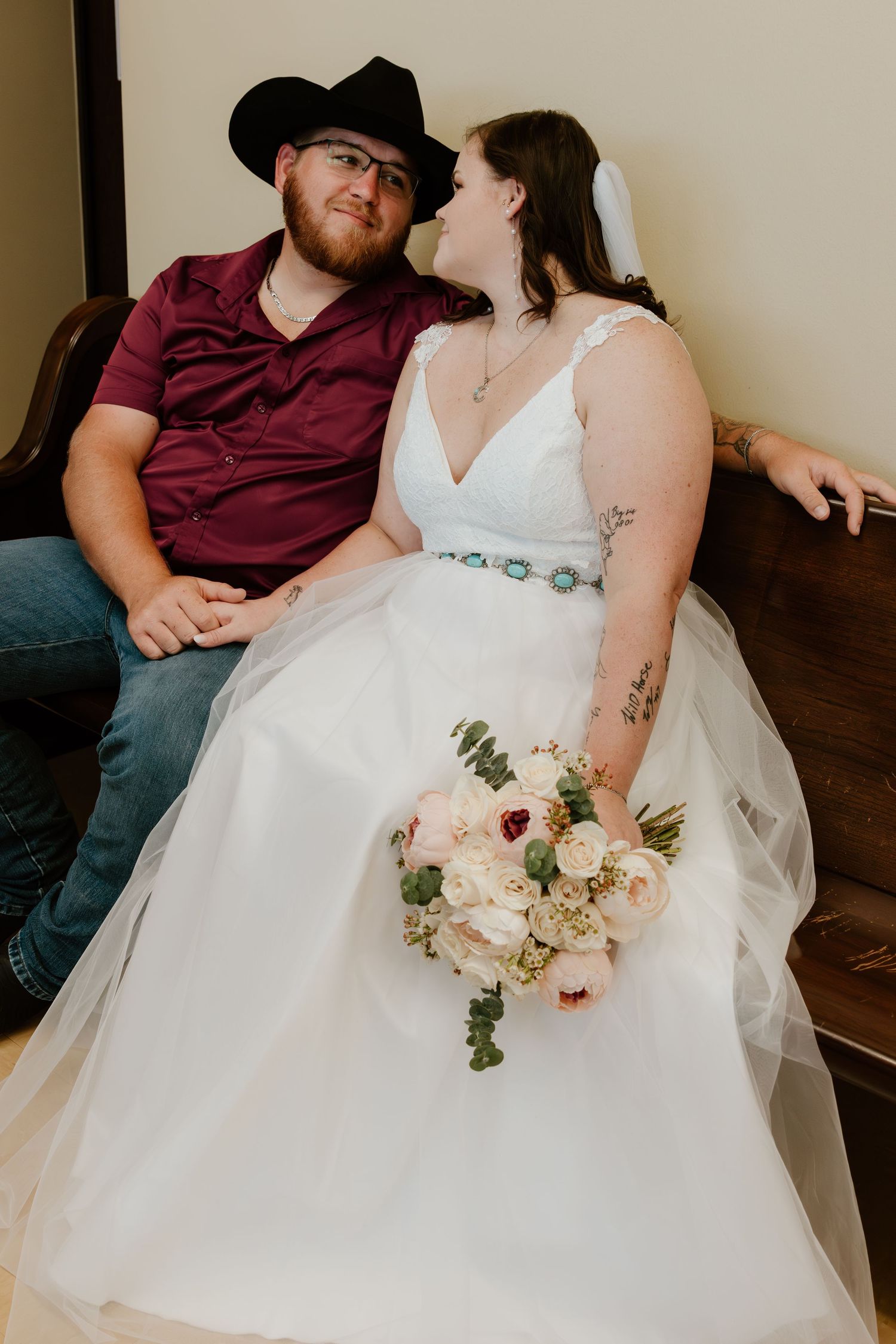 Couple sitting together with bride in white dress holding delicate floral bouquet.