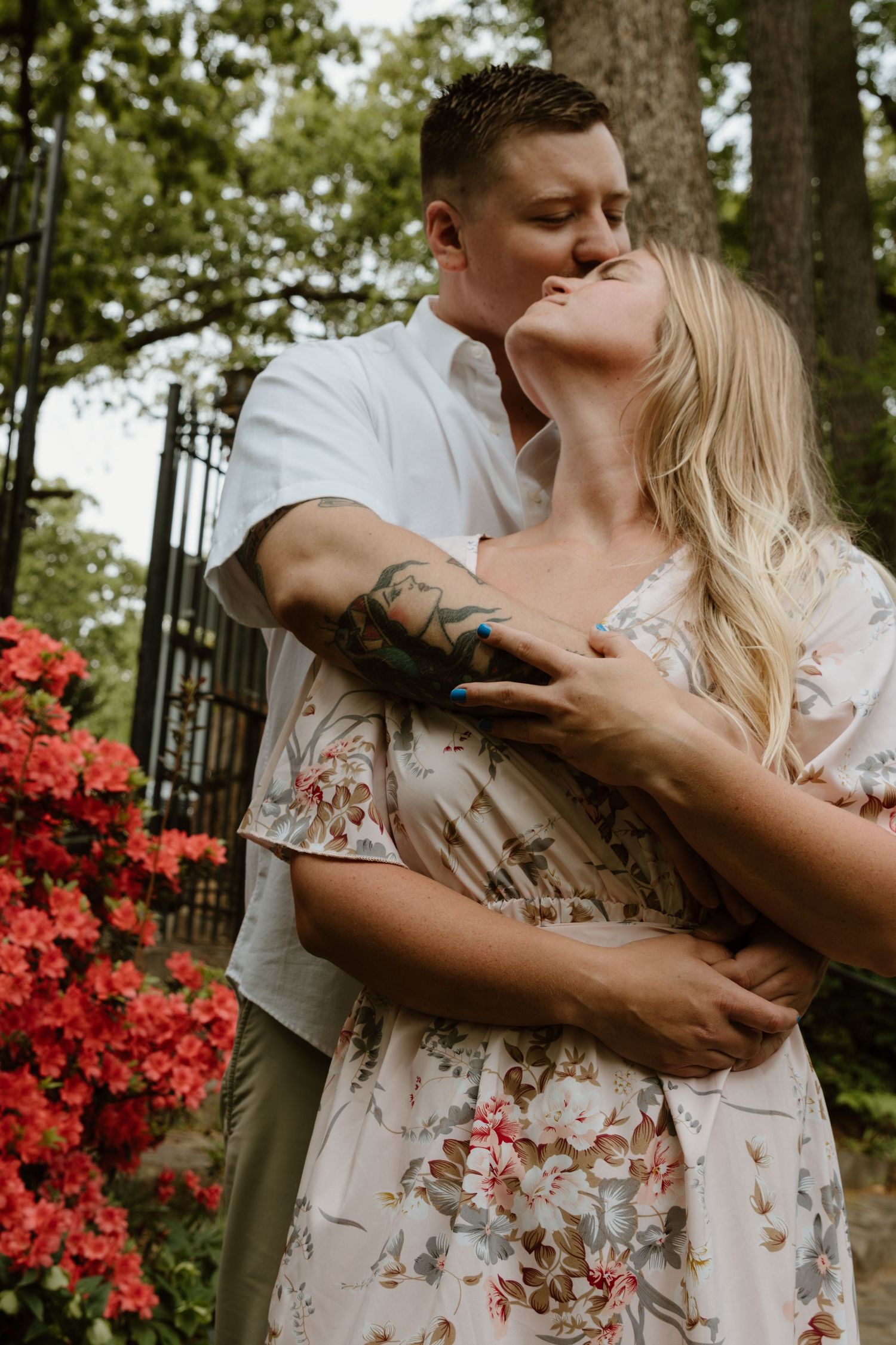 A romantic outdoor portrait with vibrant red azalea flowers in the background.